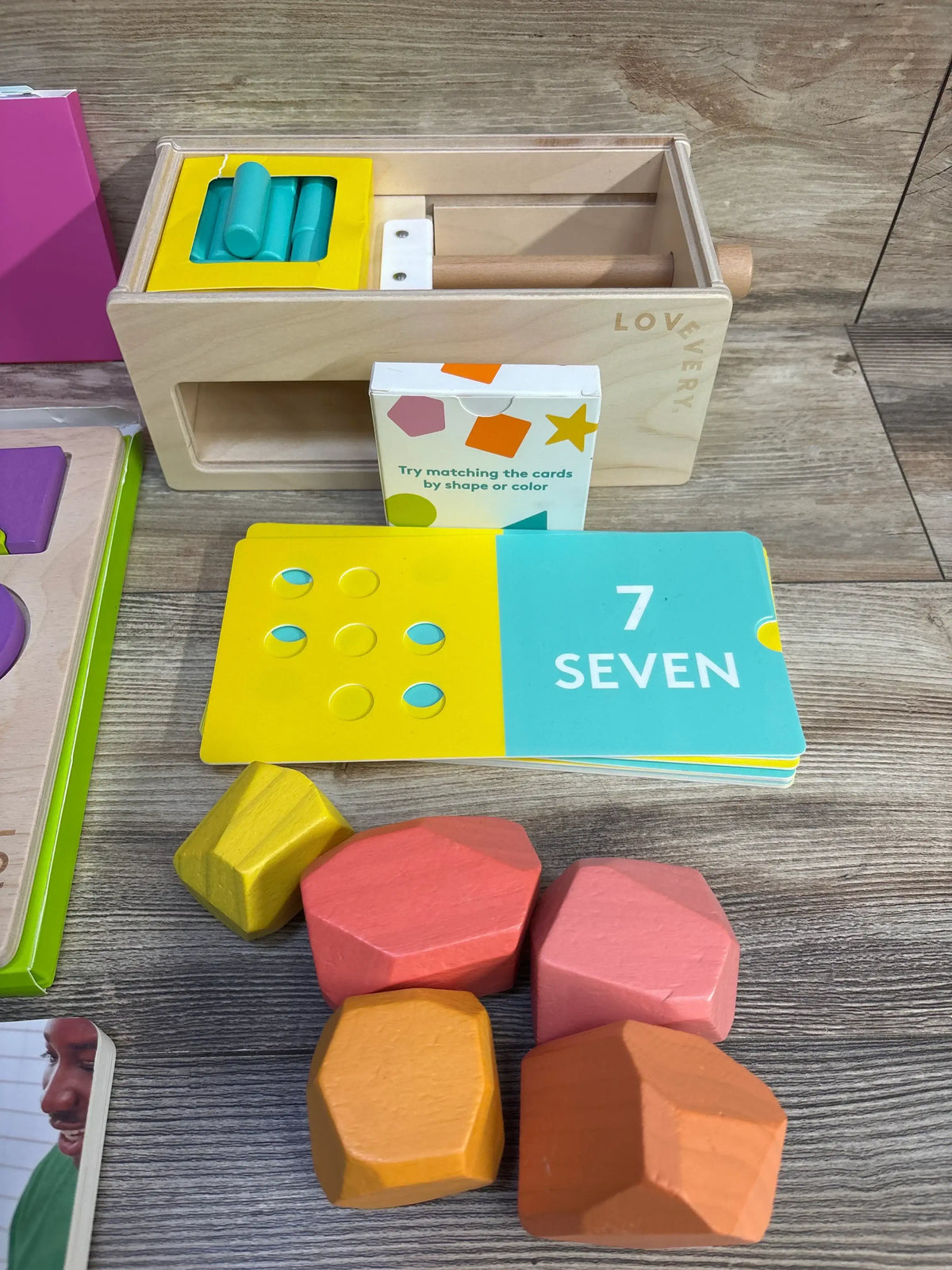 Top view of Lovevery Free Spirit Play Kit with wooden shape sorter, 7 SEVEN card and colorful wooden shapes on wood table