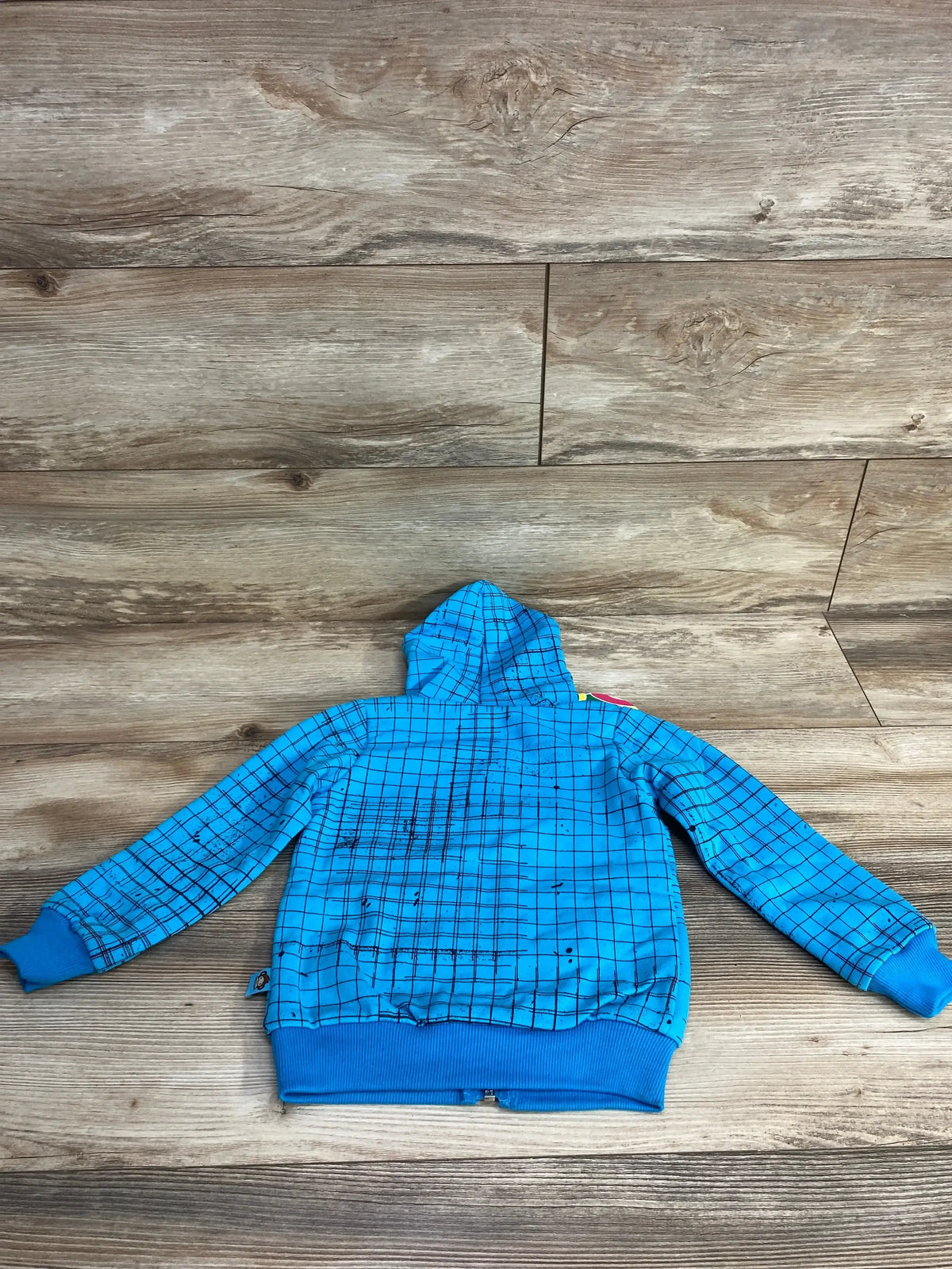 Blue children's hoodie with black grid pattern and ribbed cuffs laid flat on wood floor