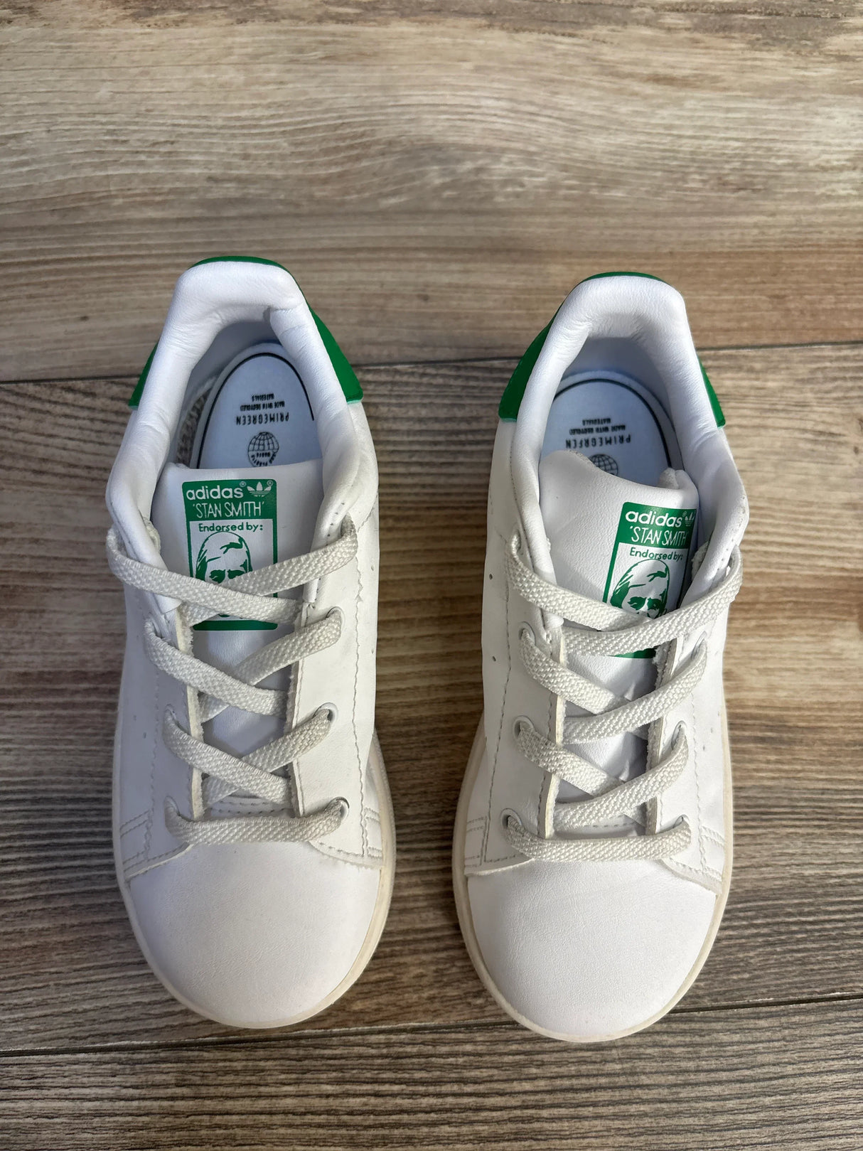Pair of white Adidas Stan Smith kids sneakers with green heel detail on wood floor