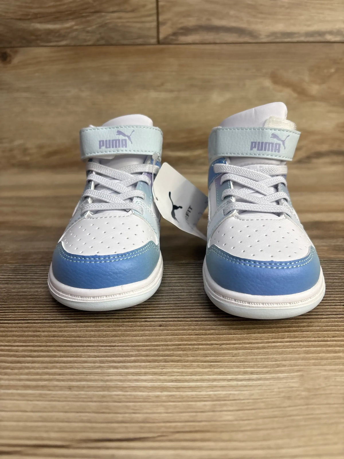 Pair of white and blue Puma toddler sneakers with Velcro straps on wooden surface