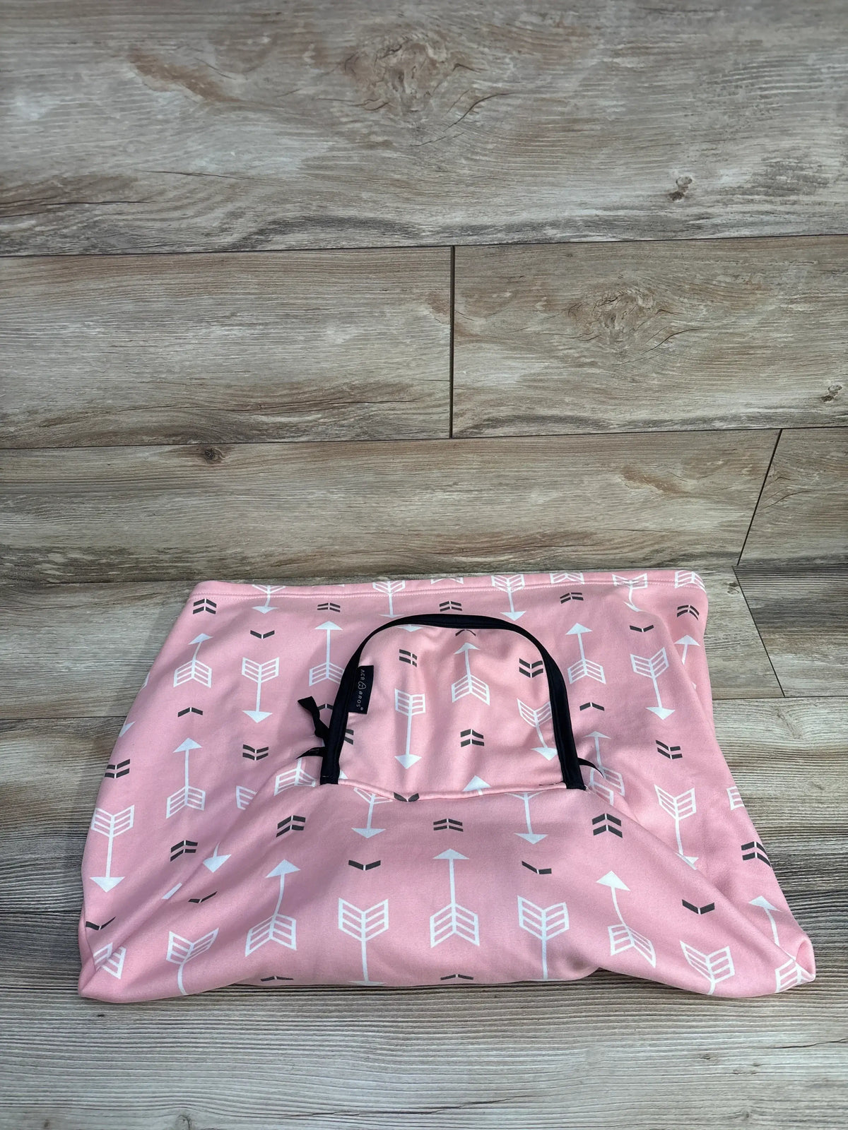Pink baby car seat cover with white and black arrow pattern on wood background