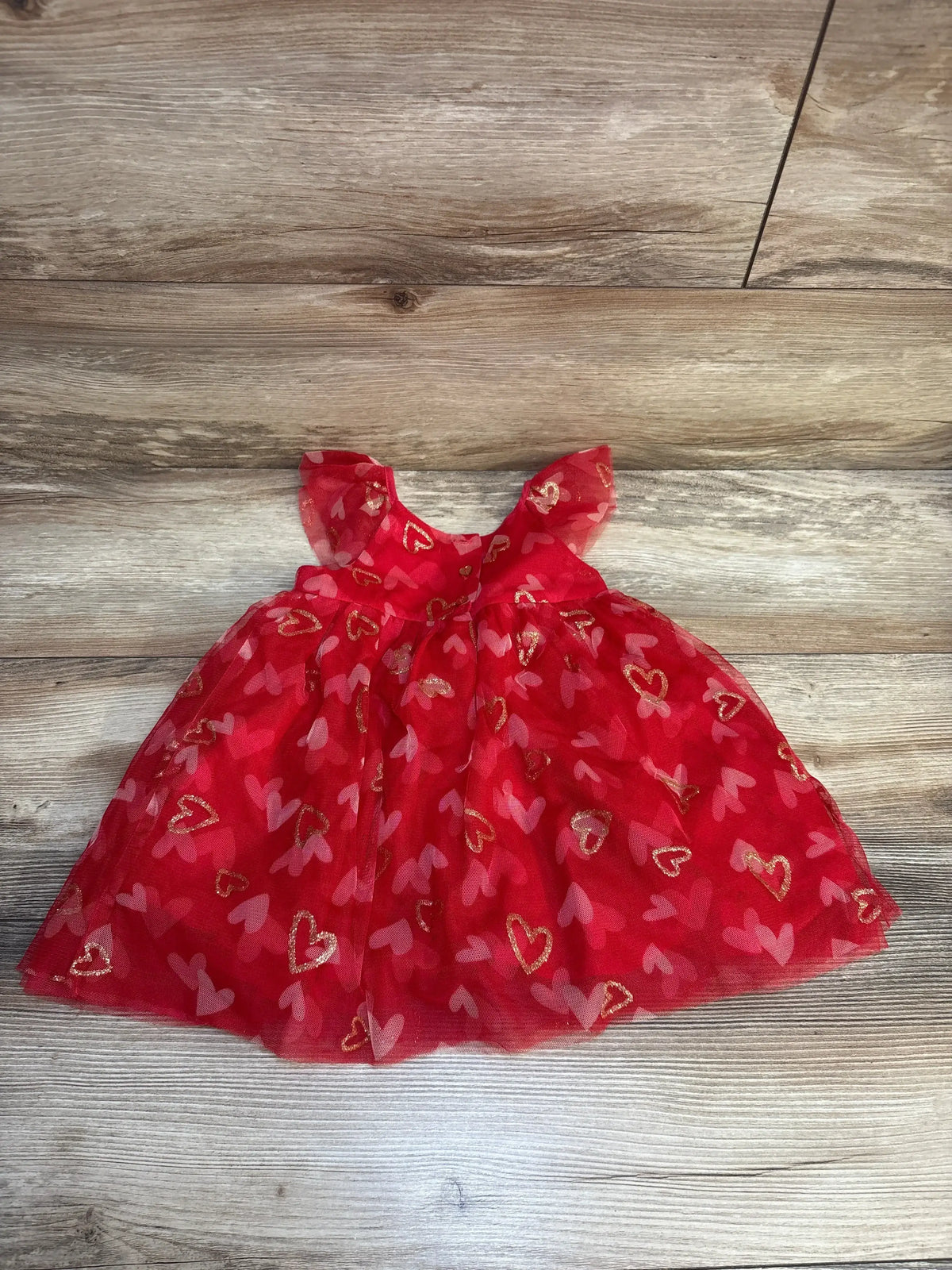 Flat lay of Isaac Mizrahi red tulle toddler dress size 18M showcasing gold glitter and pink heart prints on wood floor