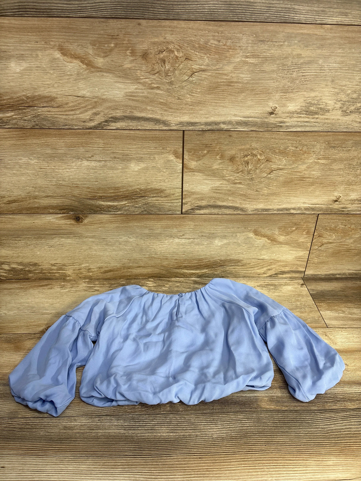 Light blue long-sleeve blouse with ruched cuffs lying flat on wooden floor