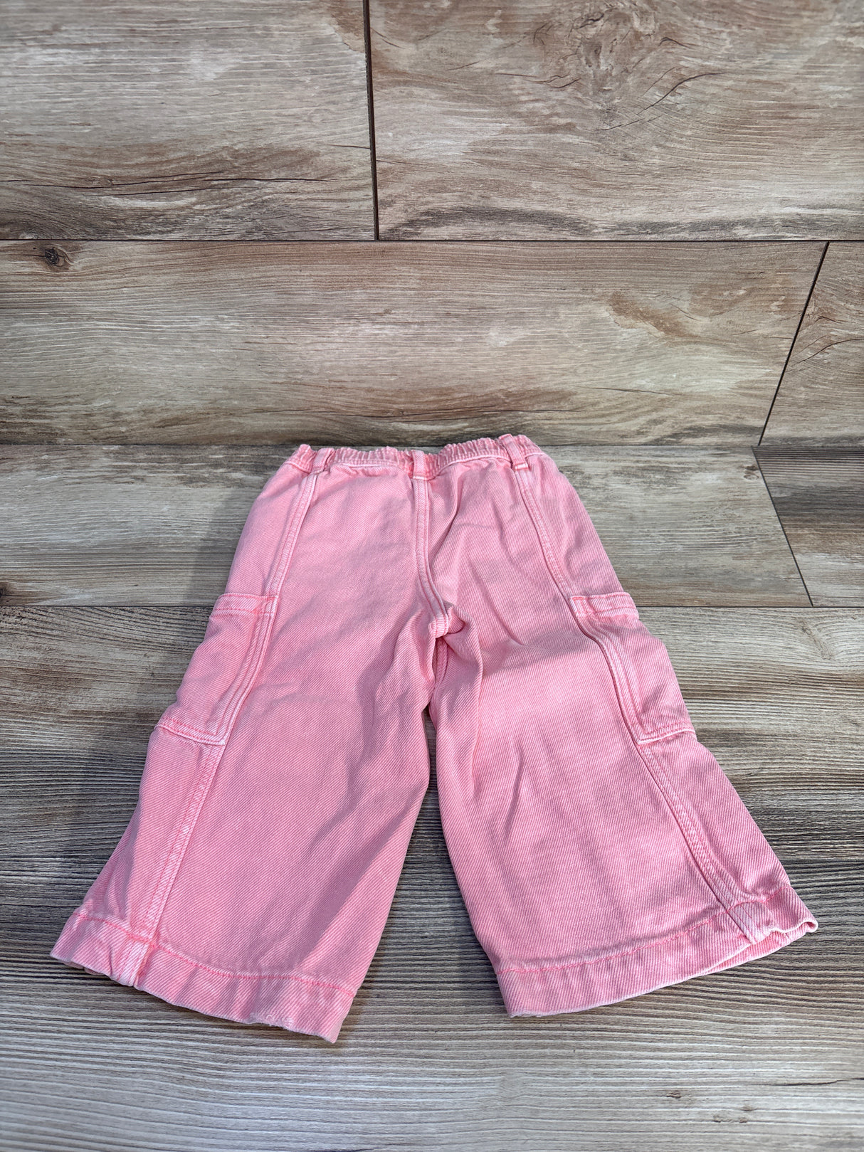 Flat lay of pink Baby Gap baggy cargo toddler jeans showcasing elastic waistband and side cargo pockets on wood floor backdrop