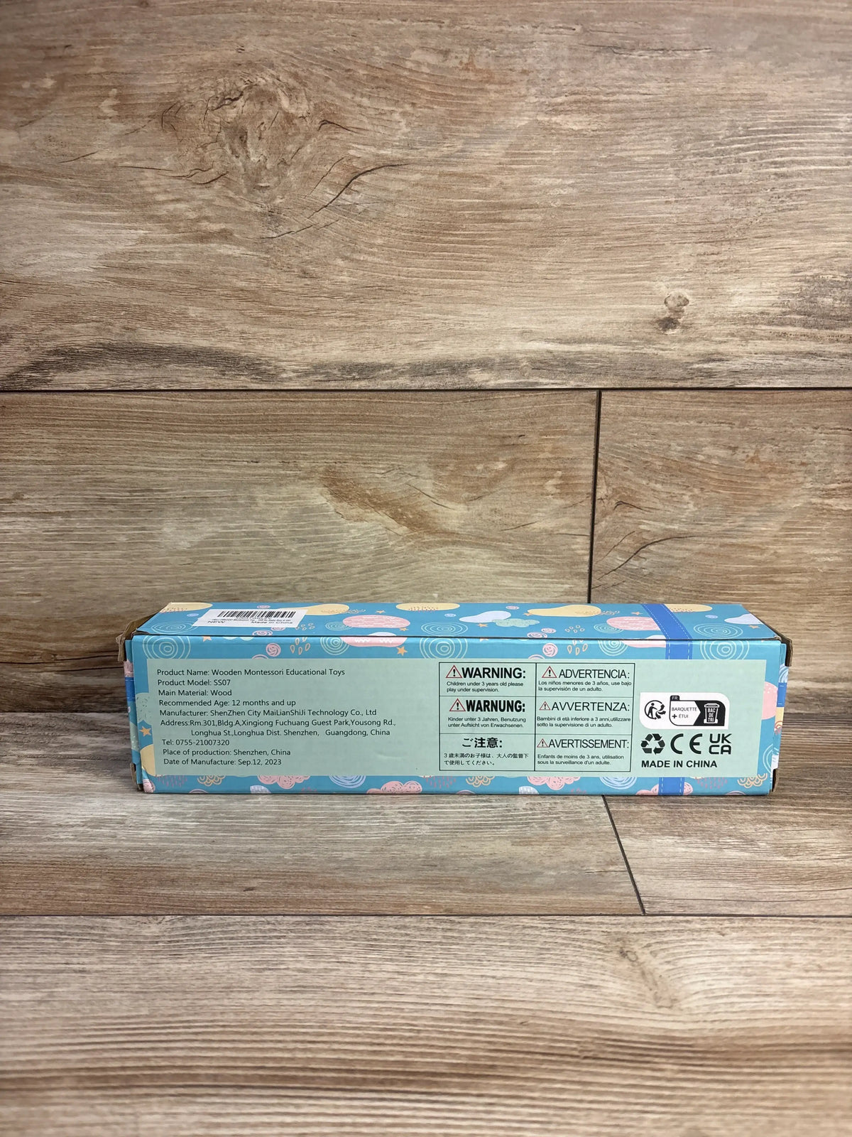 Rear view of HelloWood Montessori sorting and stacking board 20 piece set showing its colorful product box on a wood floor
