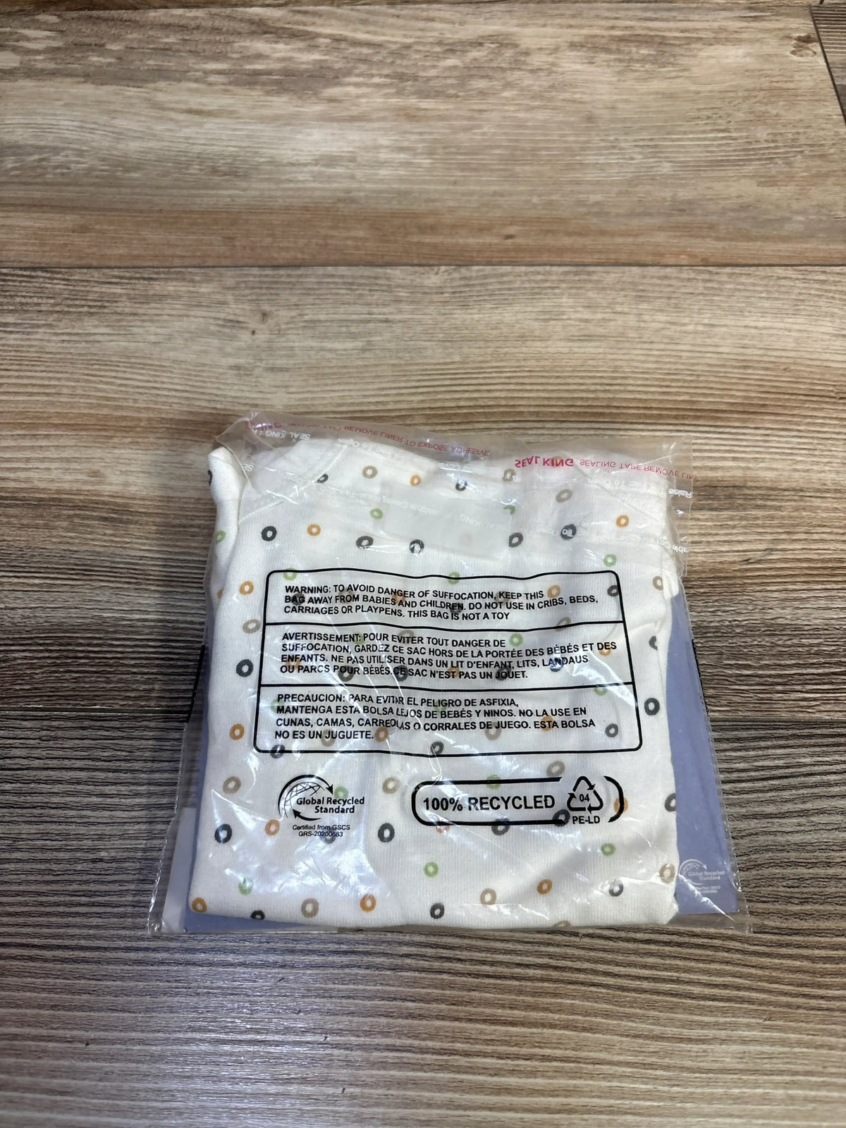 Top-down view of Small Story Cheerio bodysuit in clear packaging, showing multicolored rings on white fabric