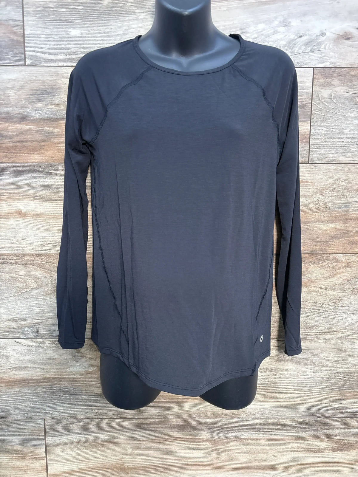 Black long sleeve athletic shirt on mannequin against wood background