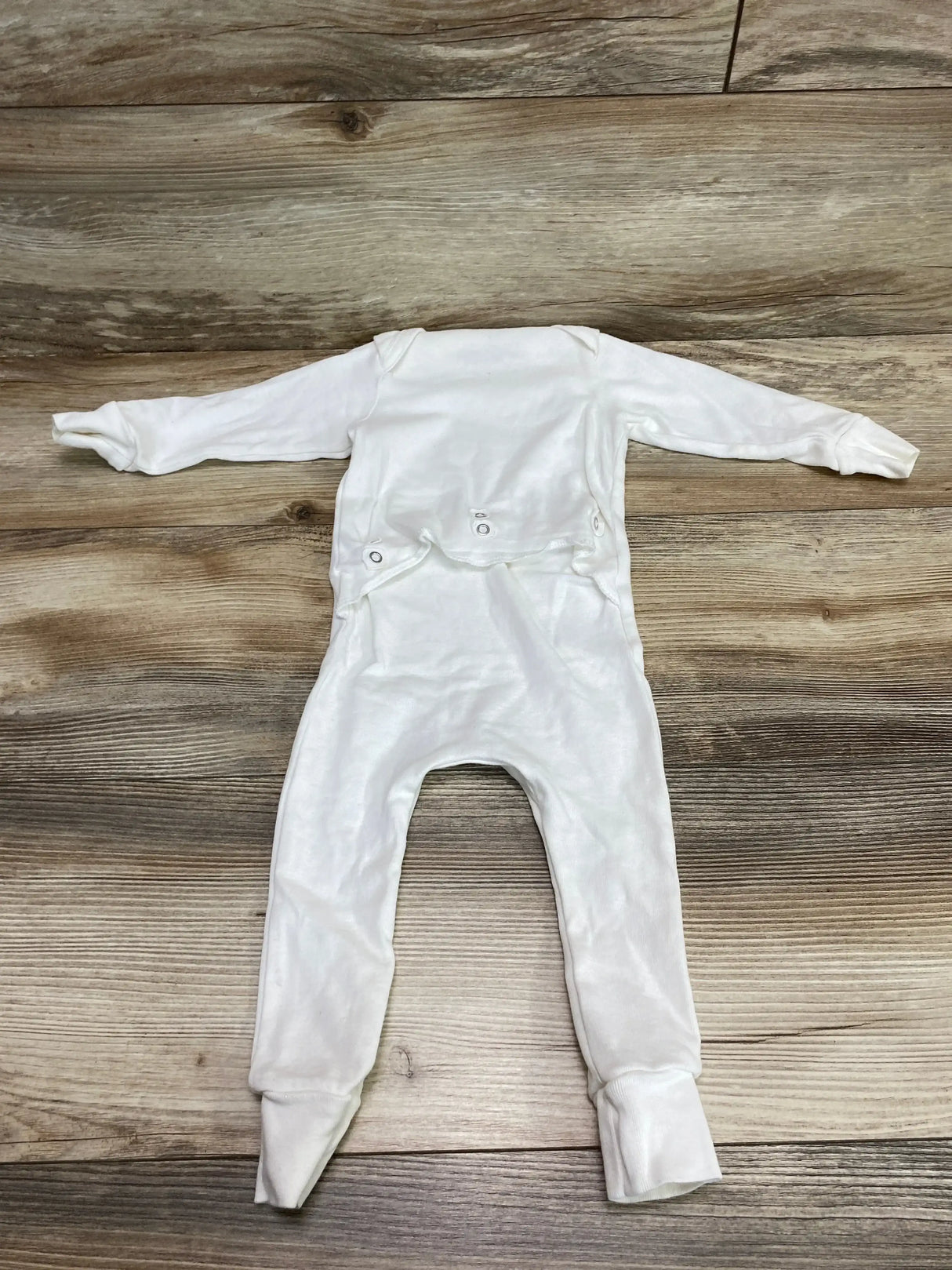 Flat lay of white Mustela footed baby pajama, size 6-12 months, showing back snap diaper flap on wood background