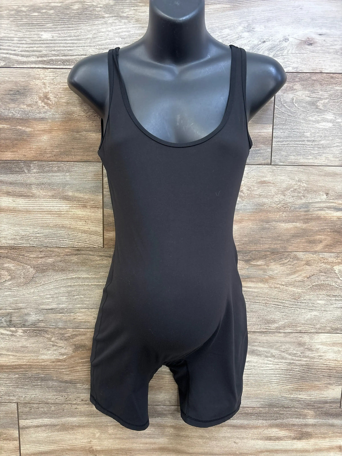 Front view of black Isabel maternity active romper showing scoop neckline, fitted belly and mid-thigh shorts on wood background