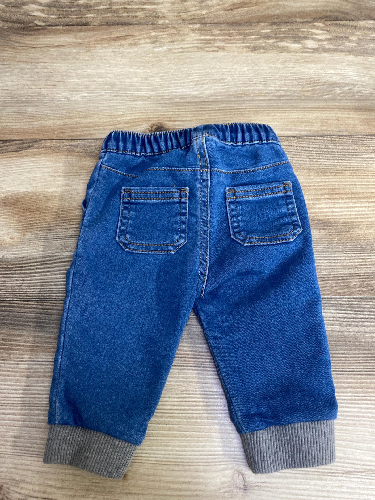 Back view of toddler blue denim jeans with elastic waist and gray ribbed cuffs on wooden floor