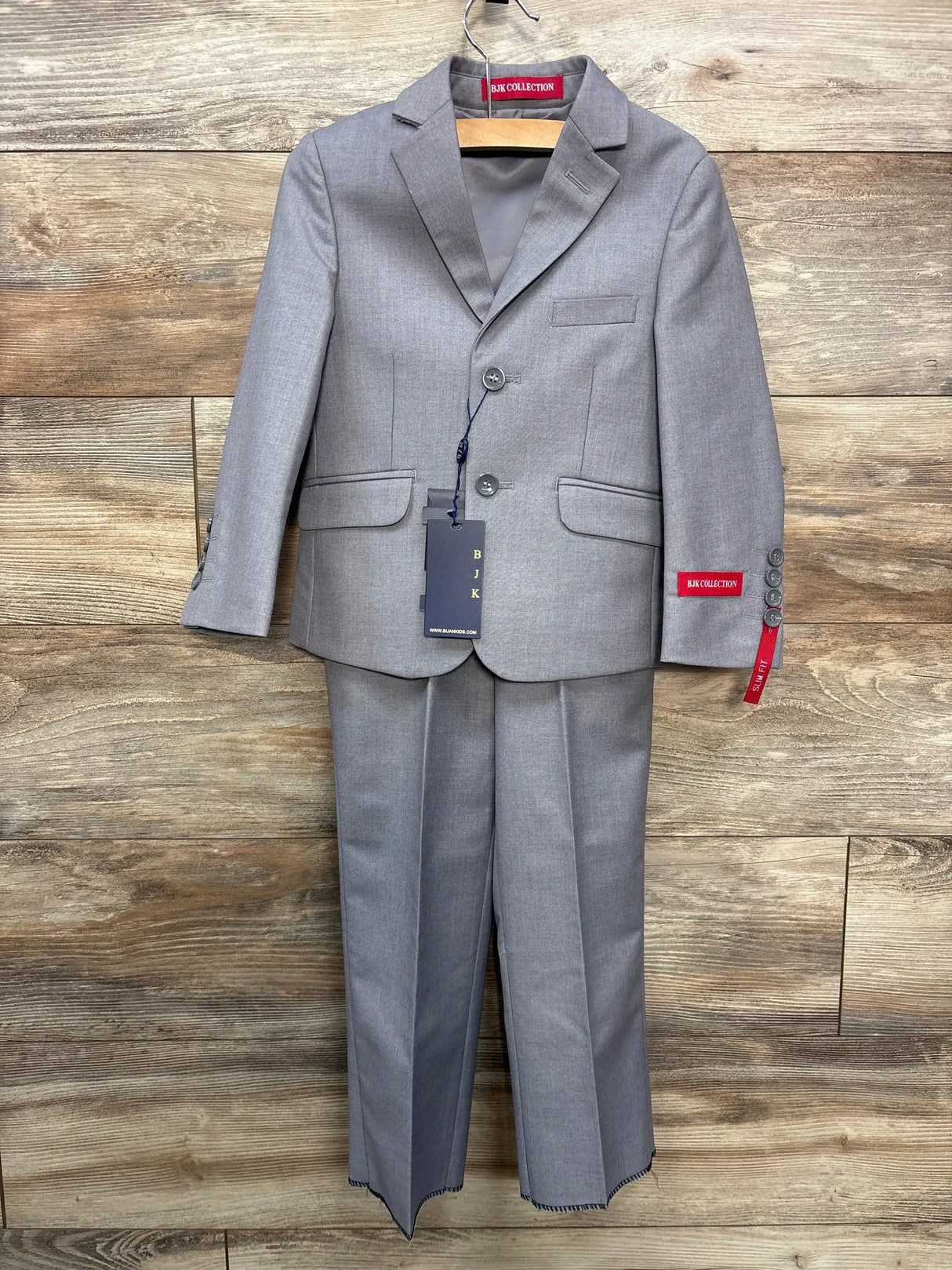 Front view of grey 3-piece toddler slim-fit suit (jacket, vest, pants) showing notch lapel and flap pockets on wood background