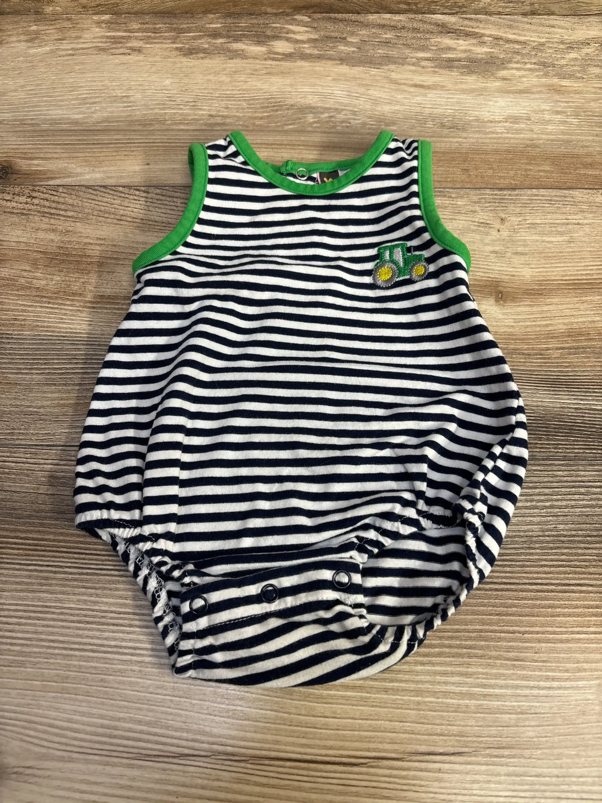 Flat lay of navy and white striped baby romper showcasing green trim, small tractor patch, and three snap crotch closures on wood surface