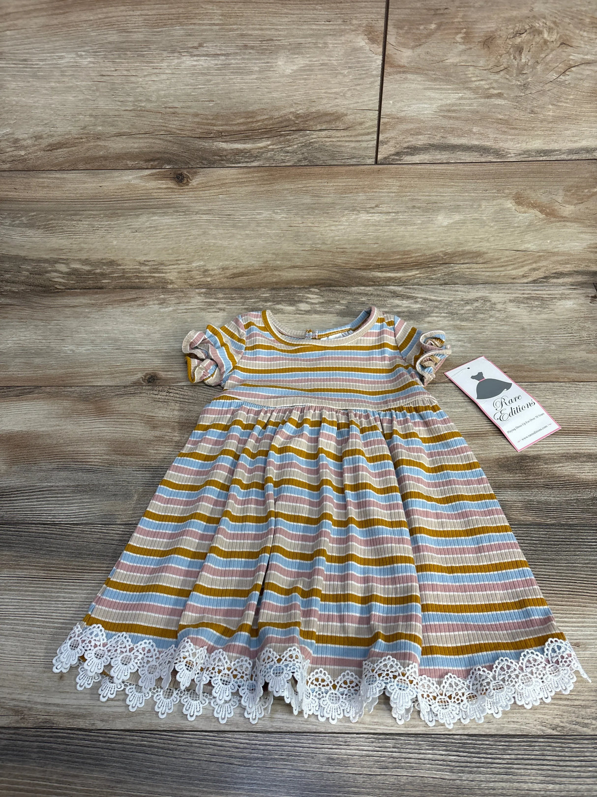 Striped baby dress with ruffled sleeves and white lace hem on wooden floor