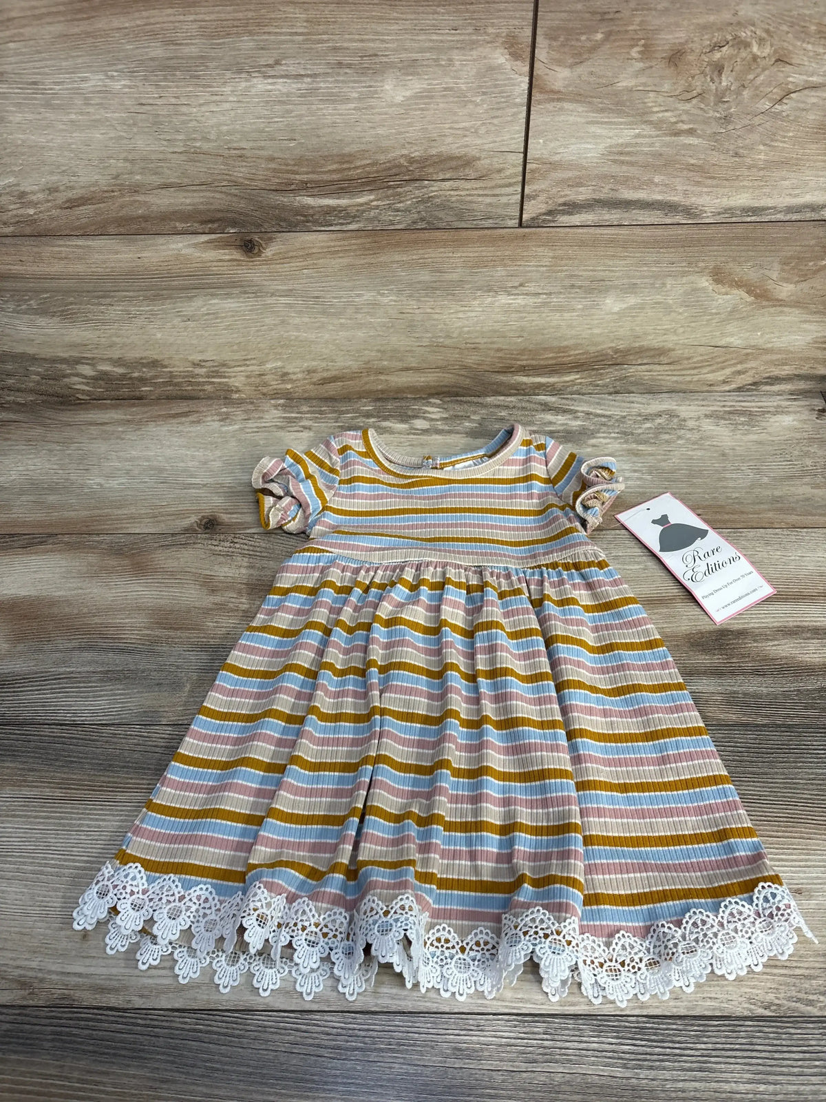 Striped baby dress with ruffled sleeves and white lace hem on wooden floor