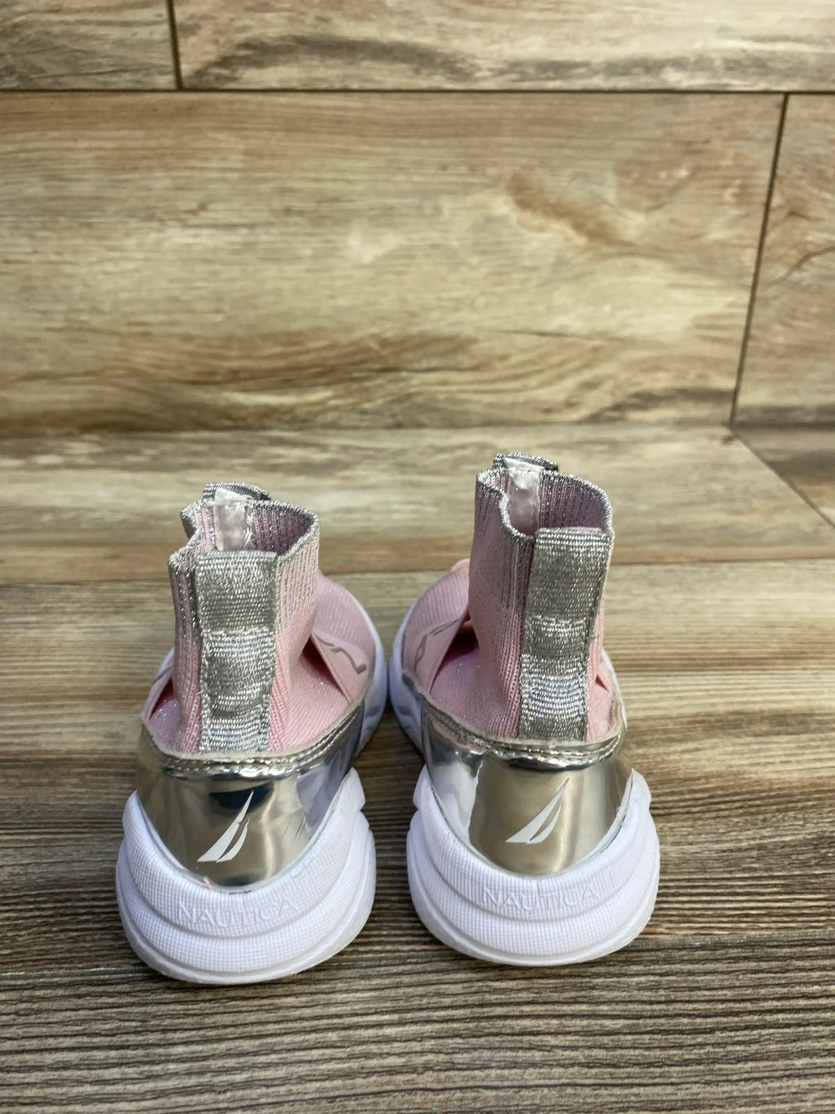 Rear view of Nautica slip-on sock-style sneakers in pink with silver accents and white soles on a wood floor