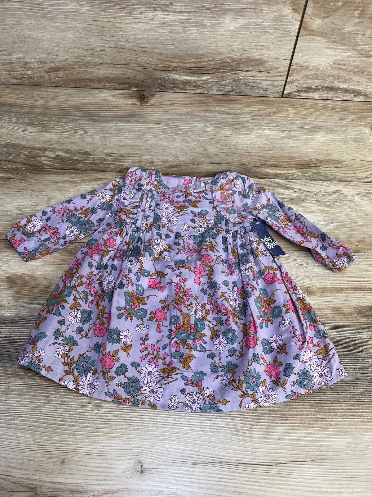Flat lay of purple OshKosh long-sleeve floral baby dress with ruffle front, size 18 months on wood floor