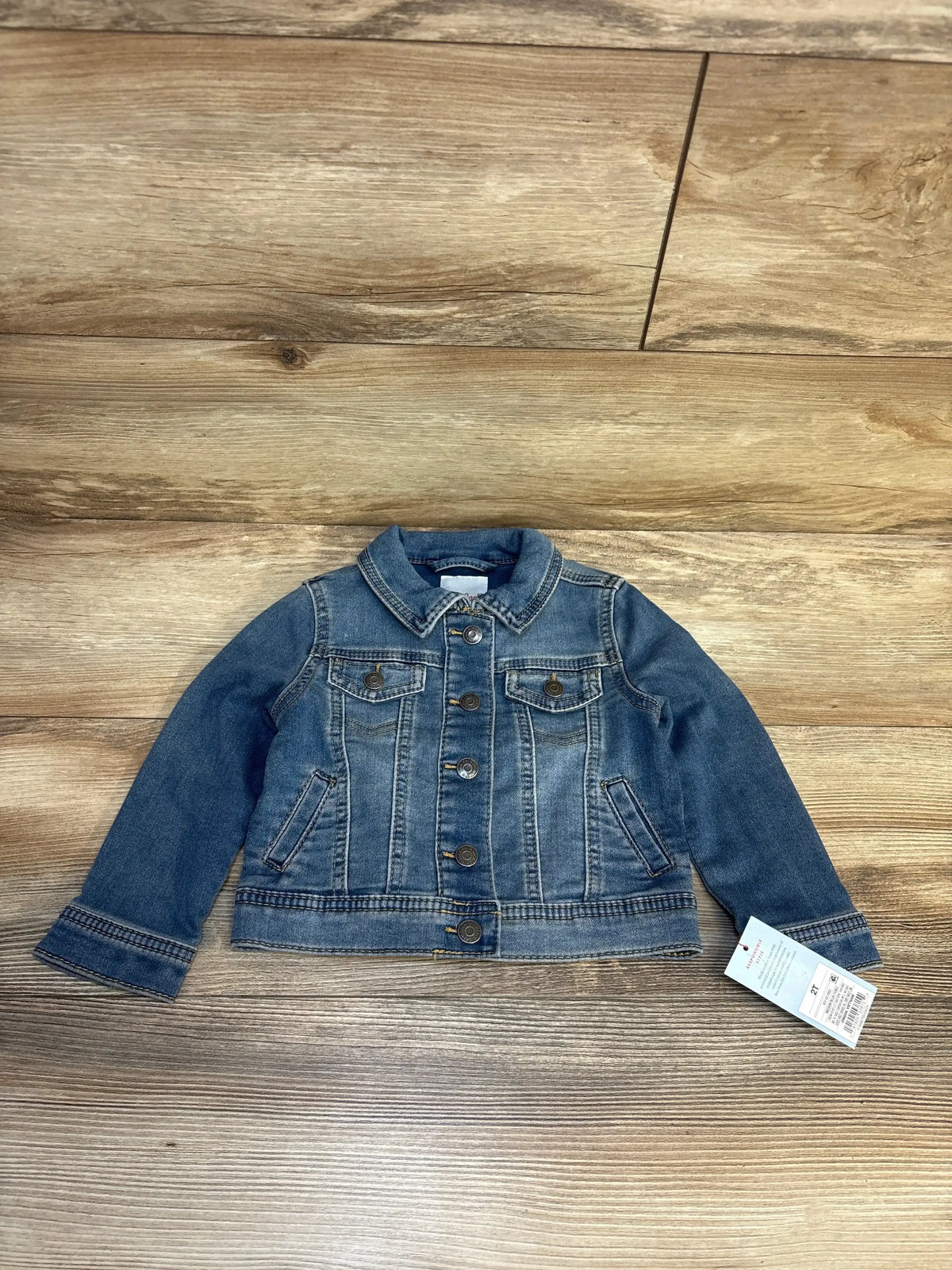 Kids blue denim jacket with button closure and front pockets on wood background
