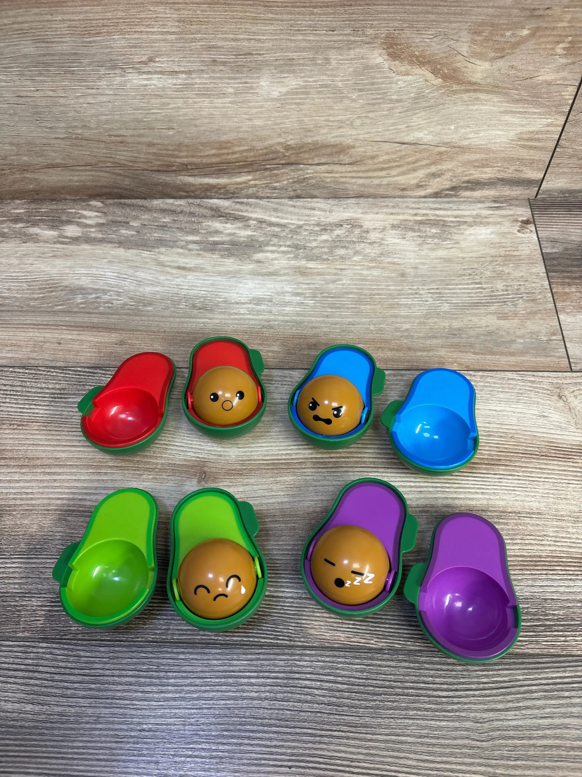 Top view of Learn-A-Lot Avocados 9pc showcasing colorful matching shells with four emoji-faced pits on a wood surface