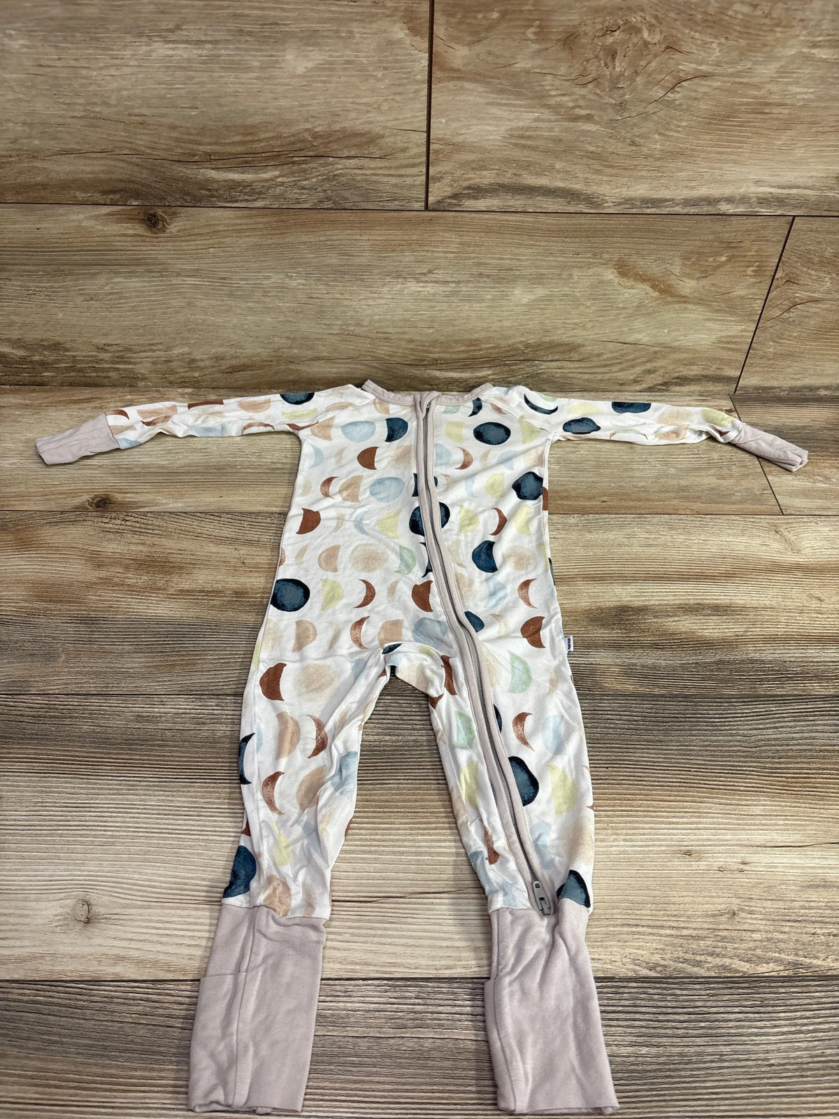 Front view of white Little Sleepies Moon Phases convertible sleeper with moon print, zipper, and fold-over cuffs on wood flooring