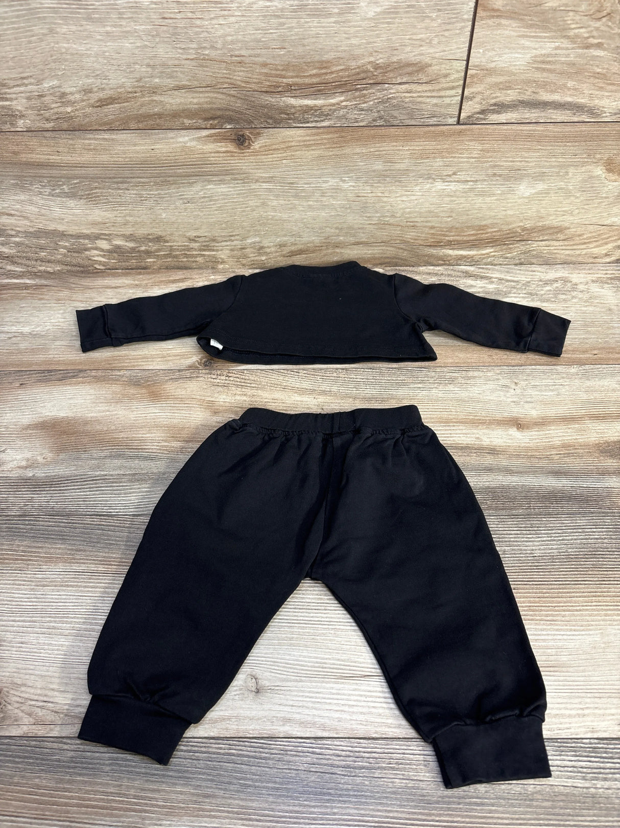 Flat lay of black 2-piece baby set: long-sleeve cropped top and elastic-waist joggers with cuffed ankles on wood background