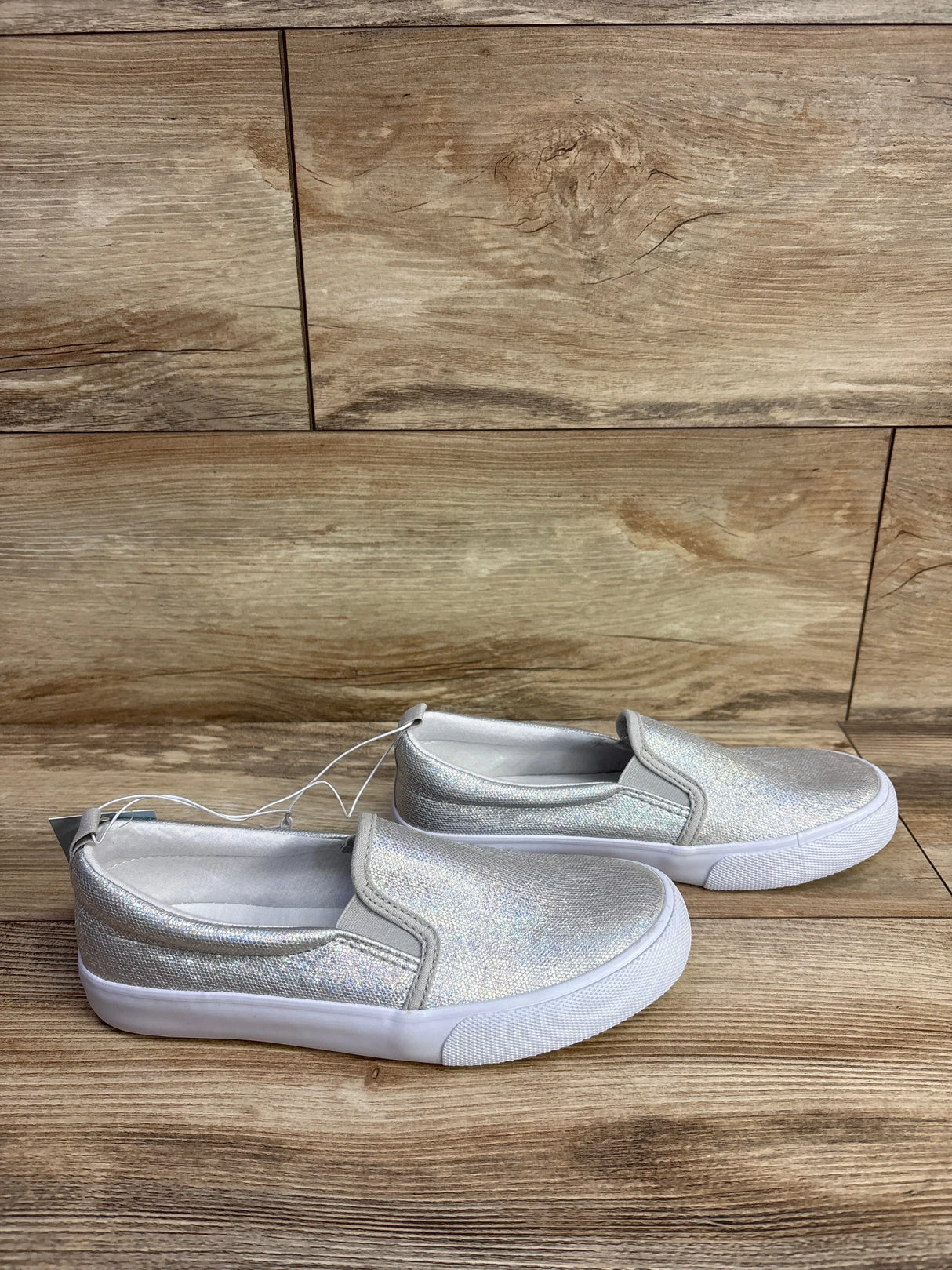 Pair of silver glitter slip-on kids shoes with white soles on wood background