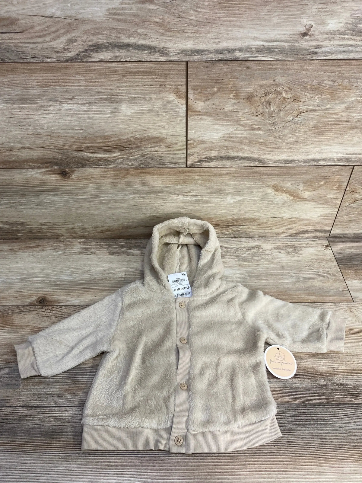 Beige plush baby hoodie jacket with buttons, long sleeves, and hood on wood background