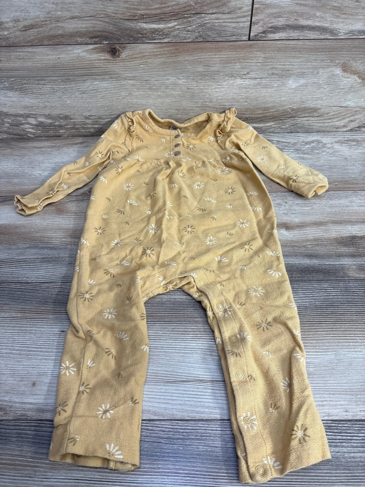 Yellow long-sleeve baby romper with white floral print laid flat on wood floor