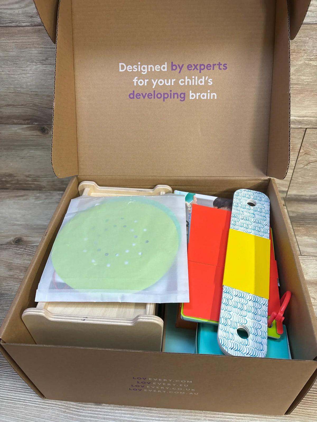 Top view of Lovevery The Analyst Play Kit open box with colorful wooden toys and cards, lid reads Designed by experts