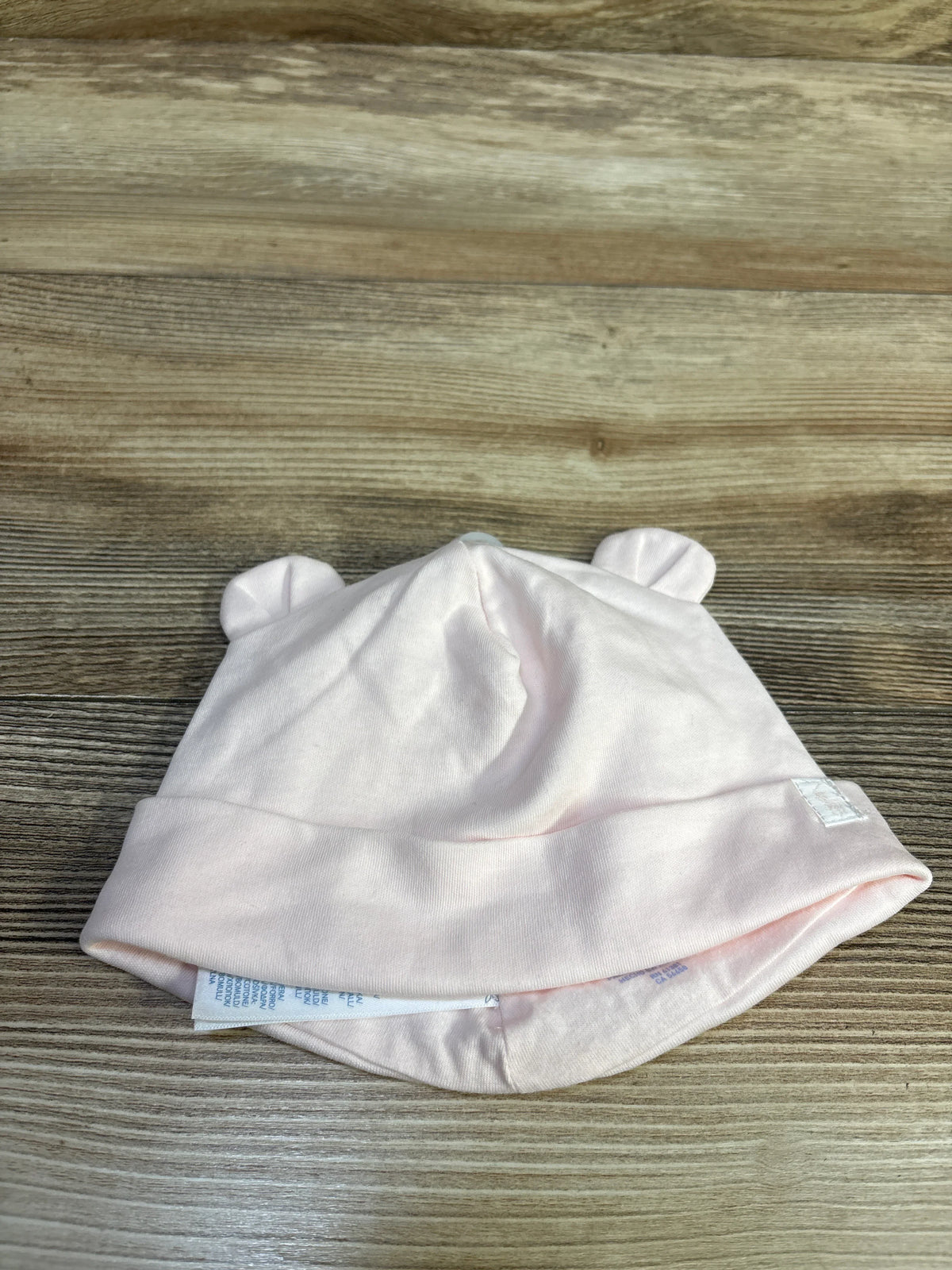 Top-down flat lay of Ralph Lauren cotton baby beanie showcasing small fabric ears and folded cuff on wooden surface