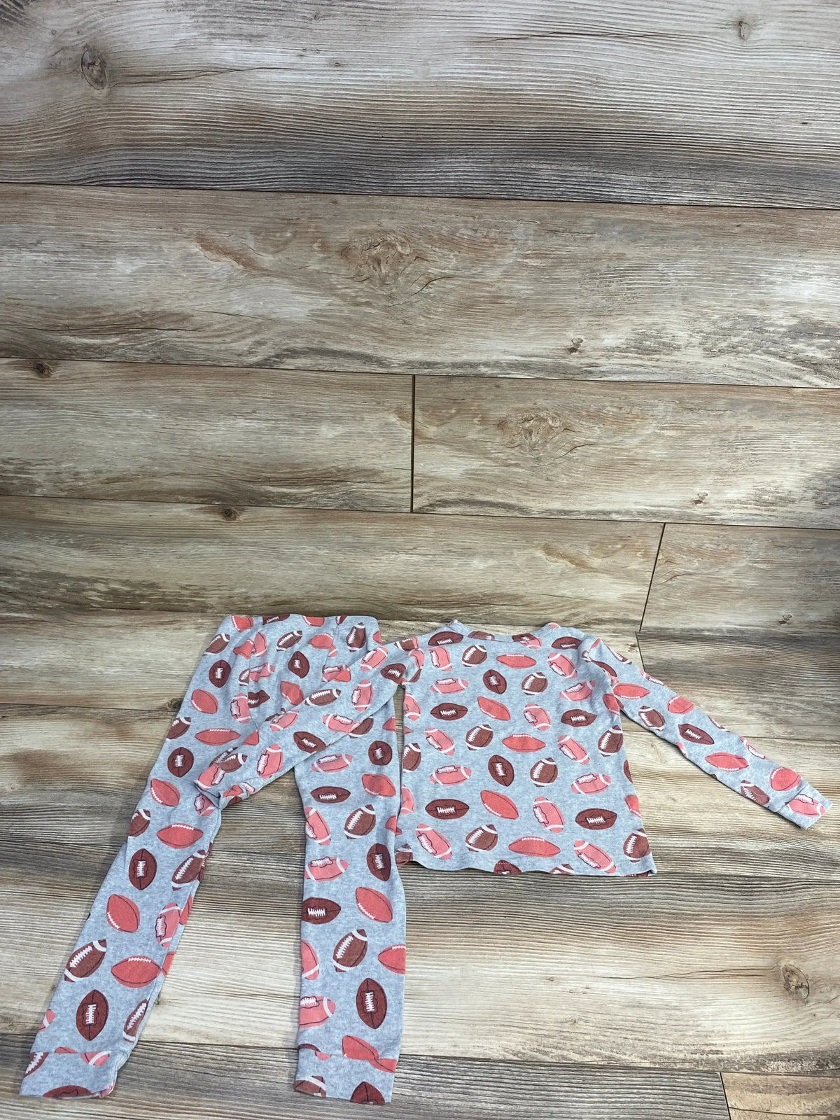 Kids grey pajama set with football print, long sleeve top and pants on wood background