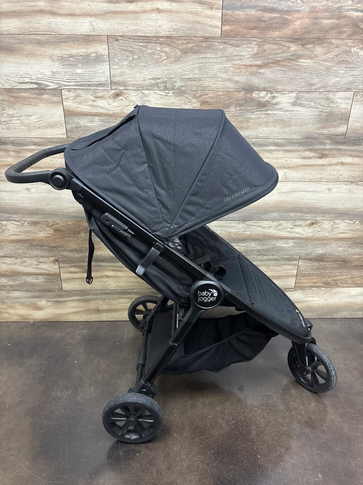 Angled view of Baby Jogger City Mini GT2 all-terrain stroller showcasing black canopy and three wheels on wood flooring