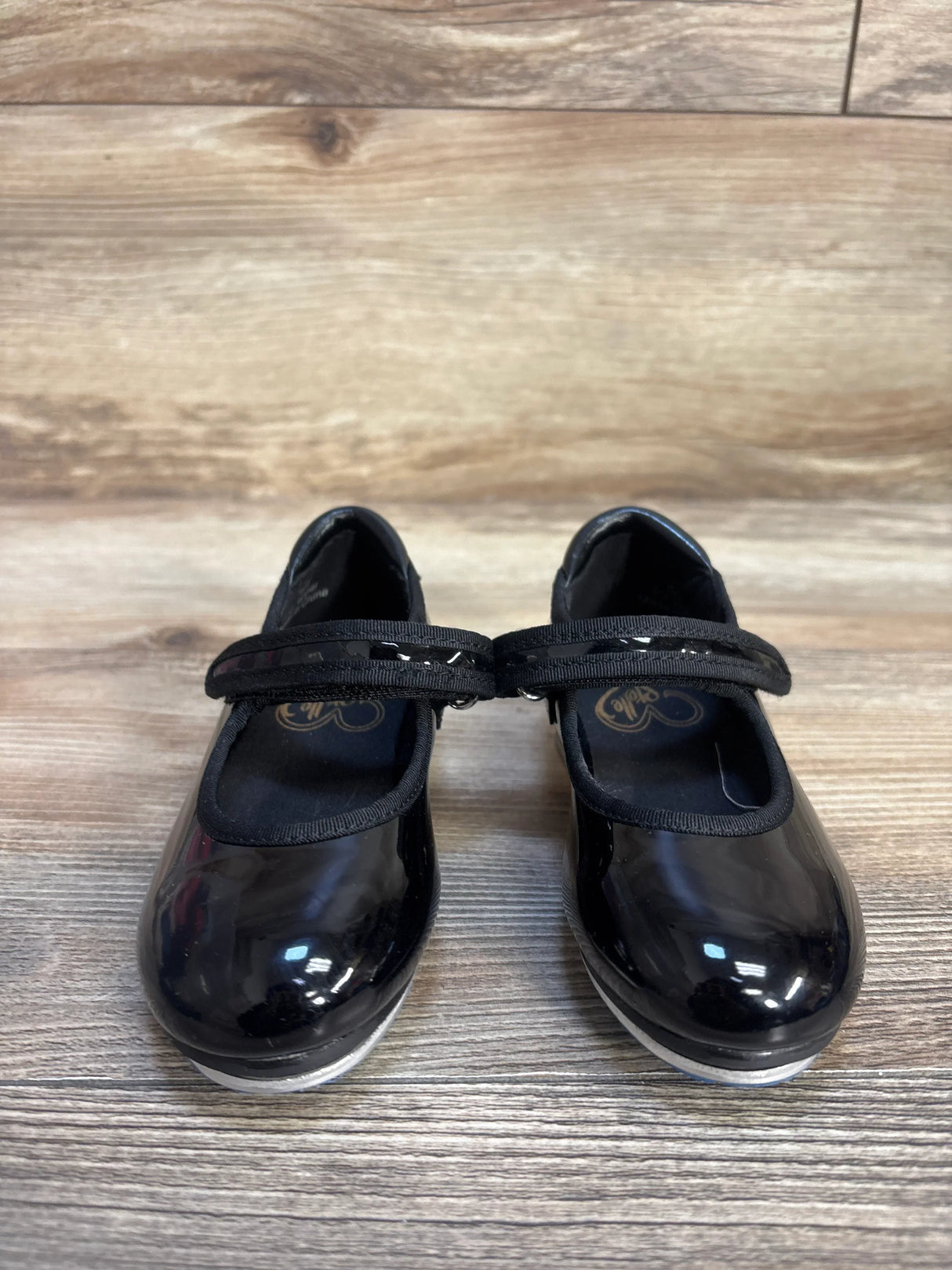 Black patent leather girls' Mary Jane shoes with Velcro strap on wood floor