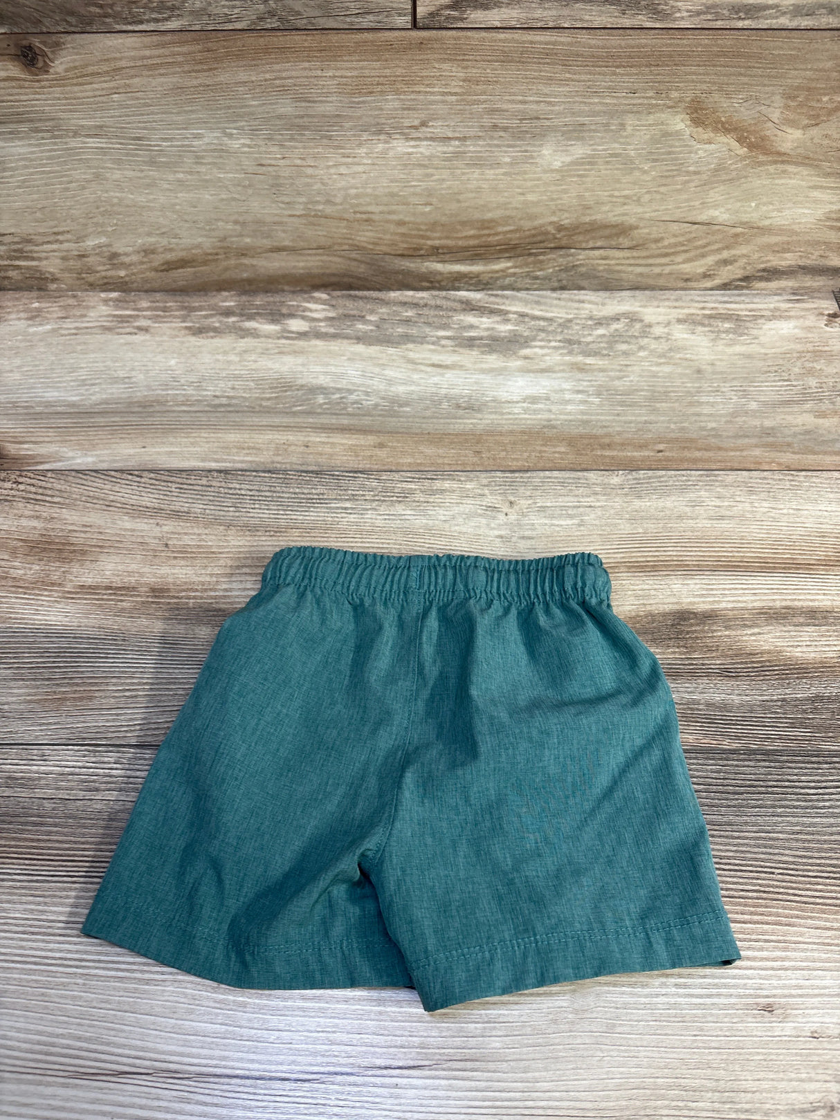 Top-down view of Tommy Bahama green board shorts size 12 months showing elastic drawstring waistband on wood background
