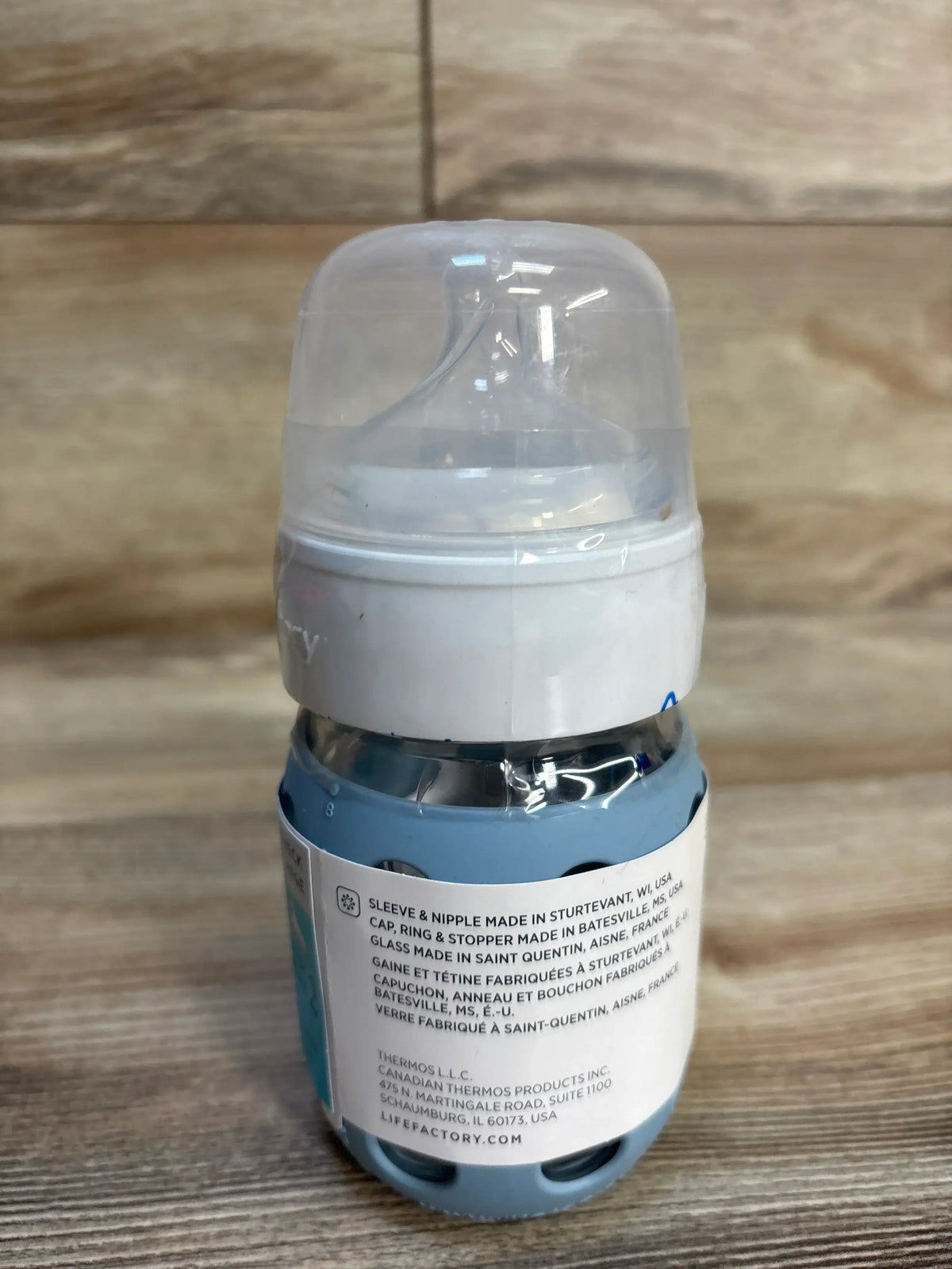 Blue baby bottle with silicone sleeve and clear cap on wood surface
