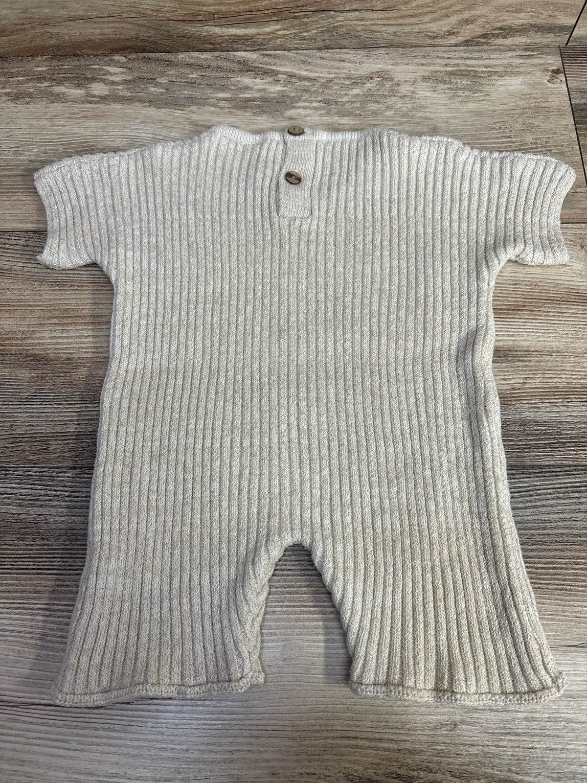 Beige ribbed knit baby romper with short sleeves and two wooden buttons on wood background