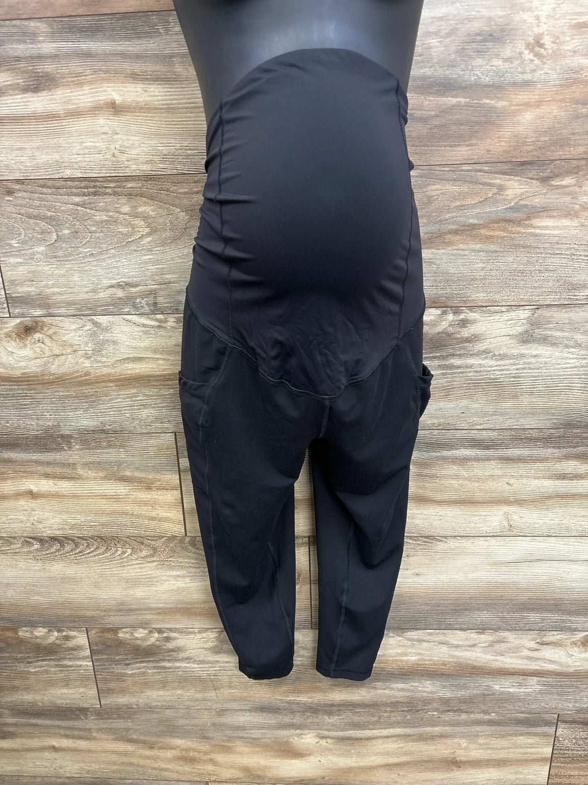 Front view of Isabel Maternity black capri leggings size Large showcasing full belly panel and side pockets on dark wood plank floor