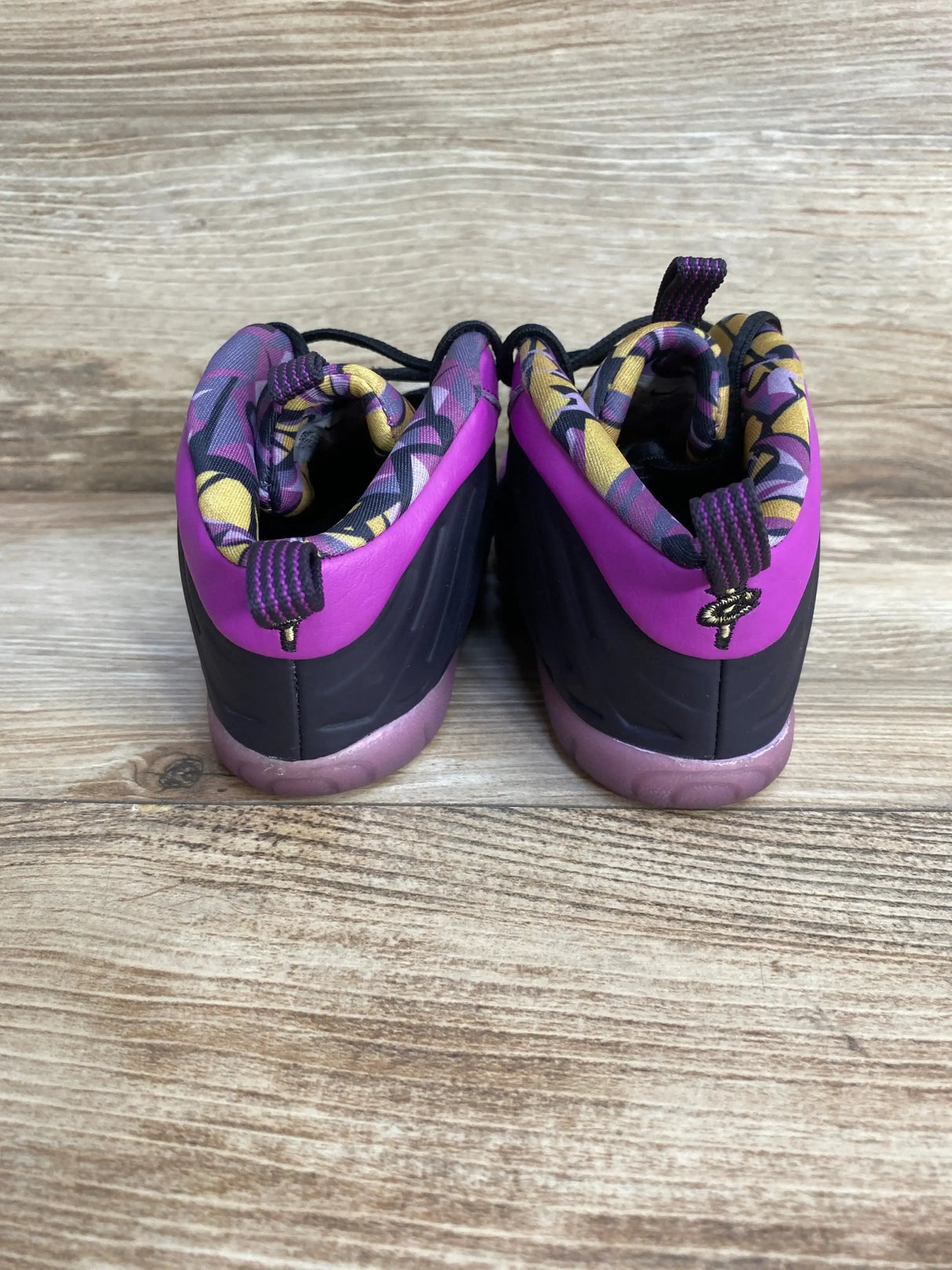 Back view of toddler Nike Little Posite One sneakers with purple heel, yellow-purple lining, pull tabs on wood floor