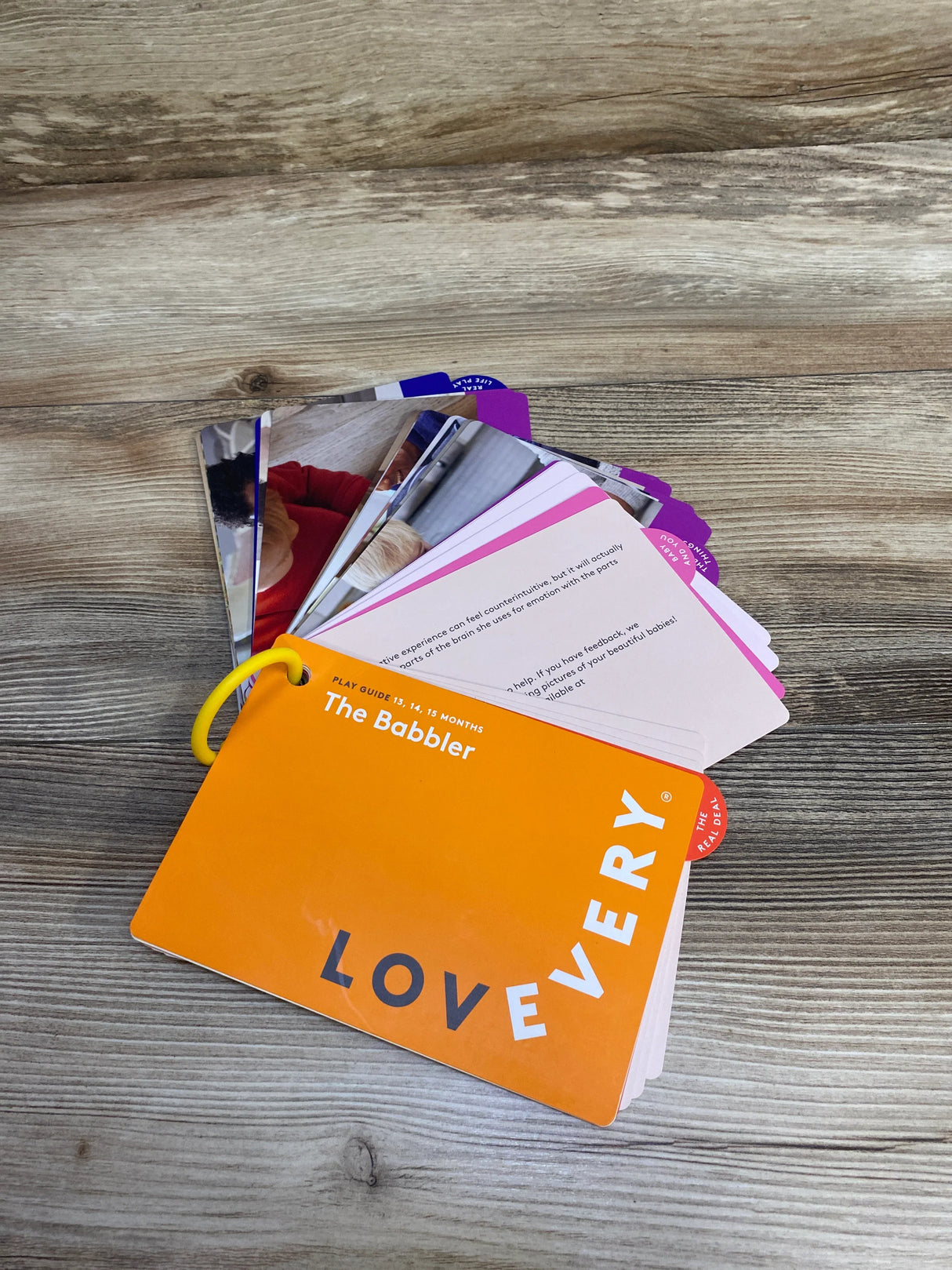 Lovevery The Babbler play guide cards for 13-15 months on wood surface