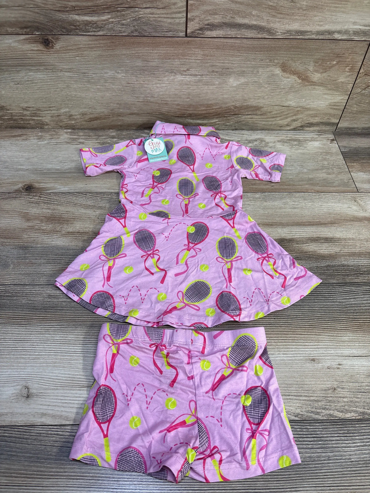 Top-down view of Gigi & Max Serena tennis polo dress and matching shorts set with pink tennis print on wood-look flooring