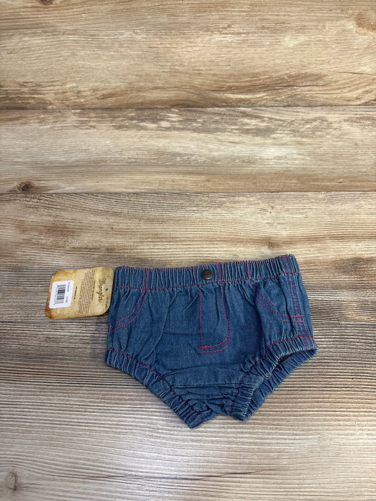 Front view of blue Wrangler denim bloomers showcasing pink stitching and elastic waistband on a wood-grain background