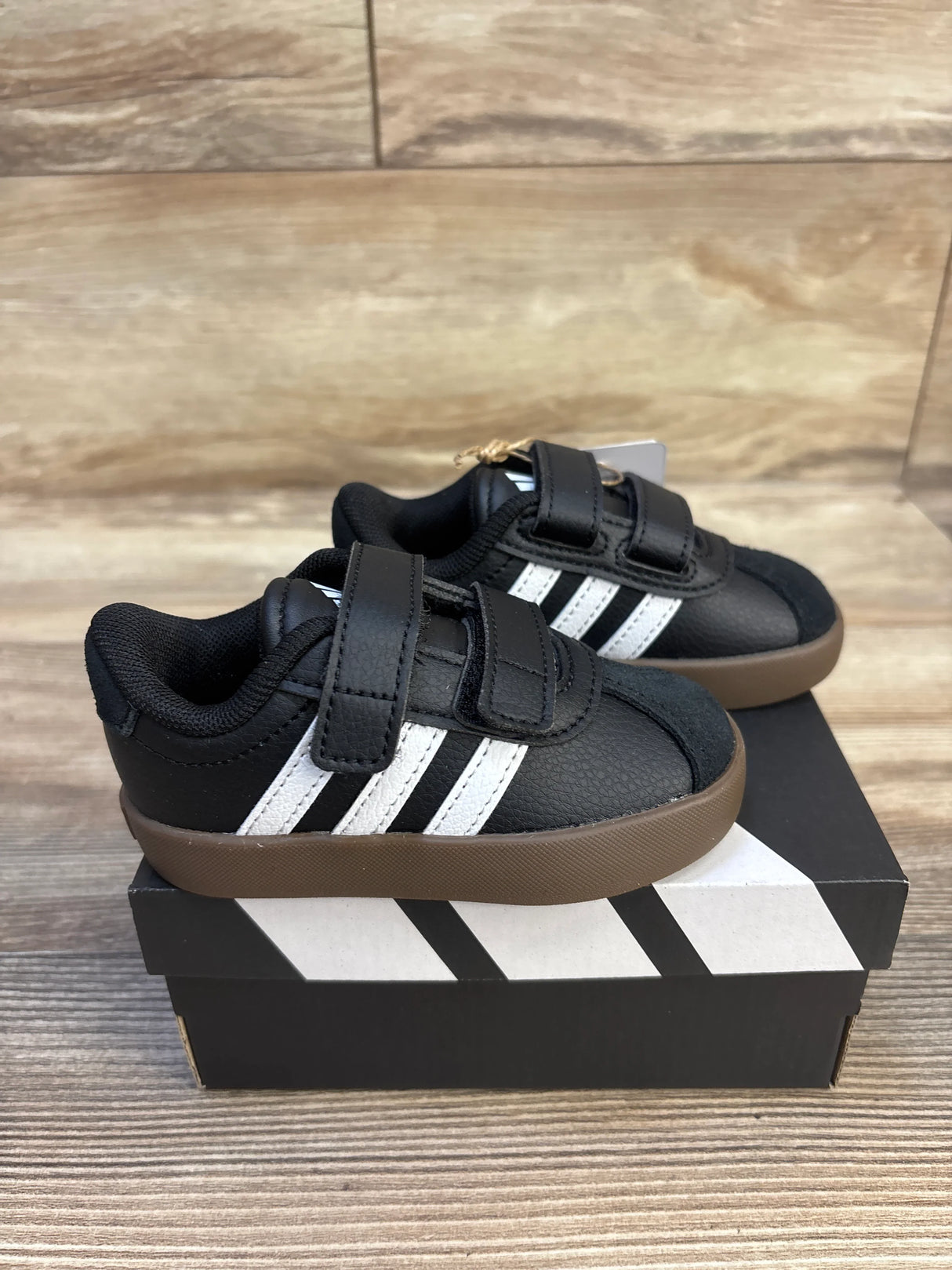 Three-quarter view of NEW Adidas VL Court 3.0 Sneakers Black sz 5c showcasing black leather upper with white stripes velcro straps and gum sole on Adidas shoebox