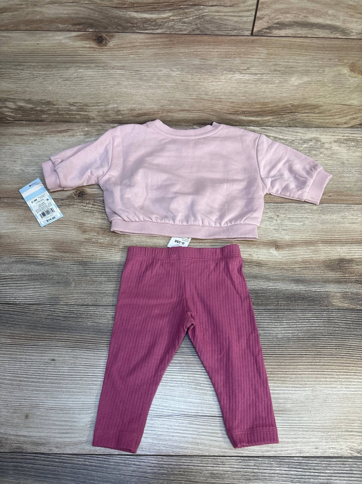 Pink baby outfit with long sleeve top and ribbed leggings on wood background