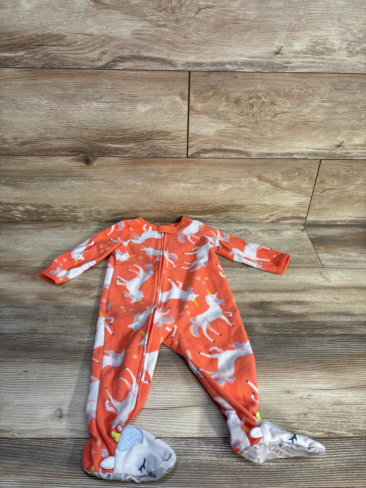 Front view of Child of Mine coral unicorn blanket sleeper with front zipper and footed design on wood-look floor