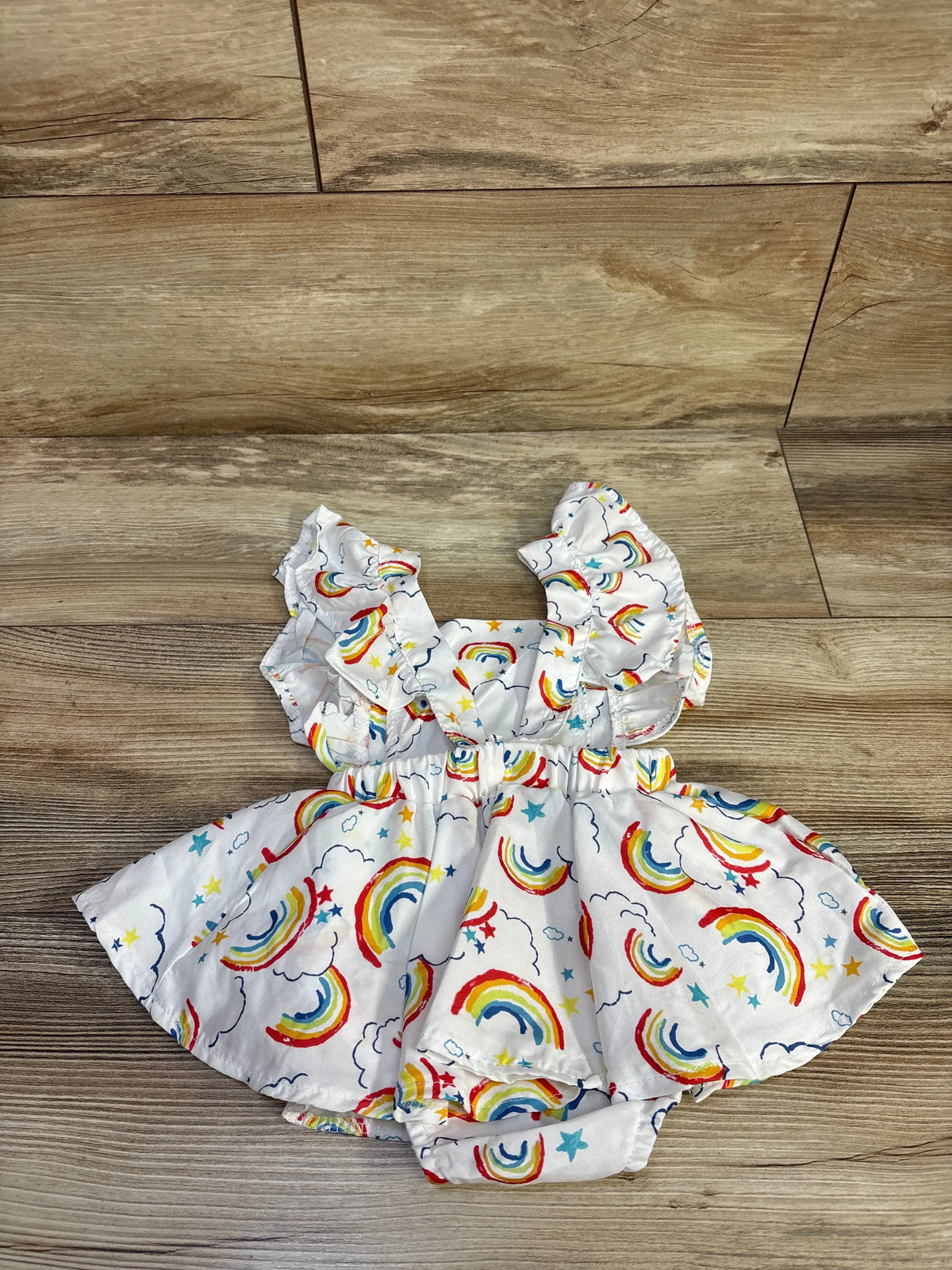 Front view of white rainbow-print bodysuit dress with ruffled sleeves and star details on a wood-look floor