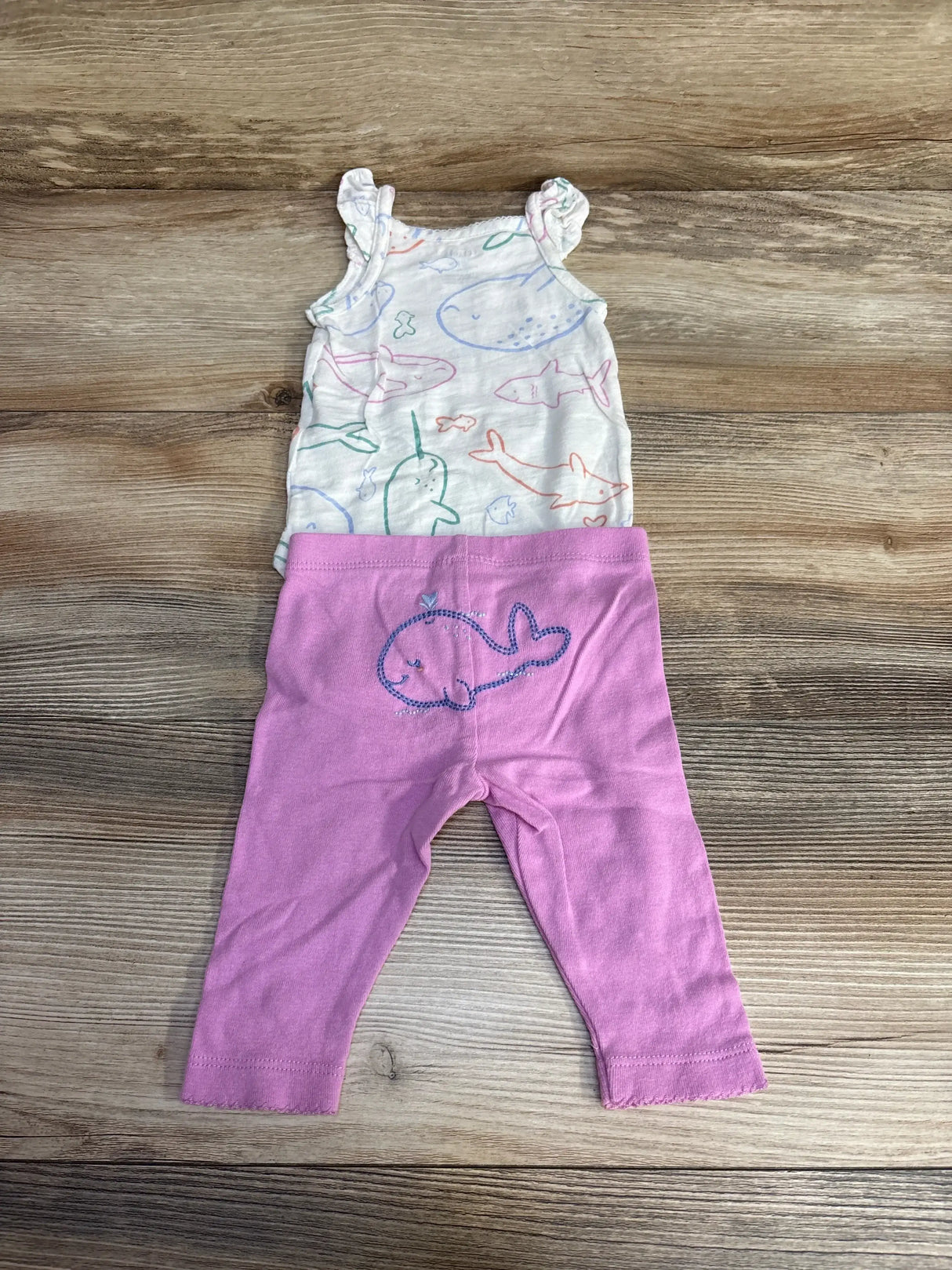 Flat lay of Carter’s 2-piece whale print bodysuit and pink leggings with ruffled straps and embroidered whale on wood