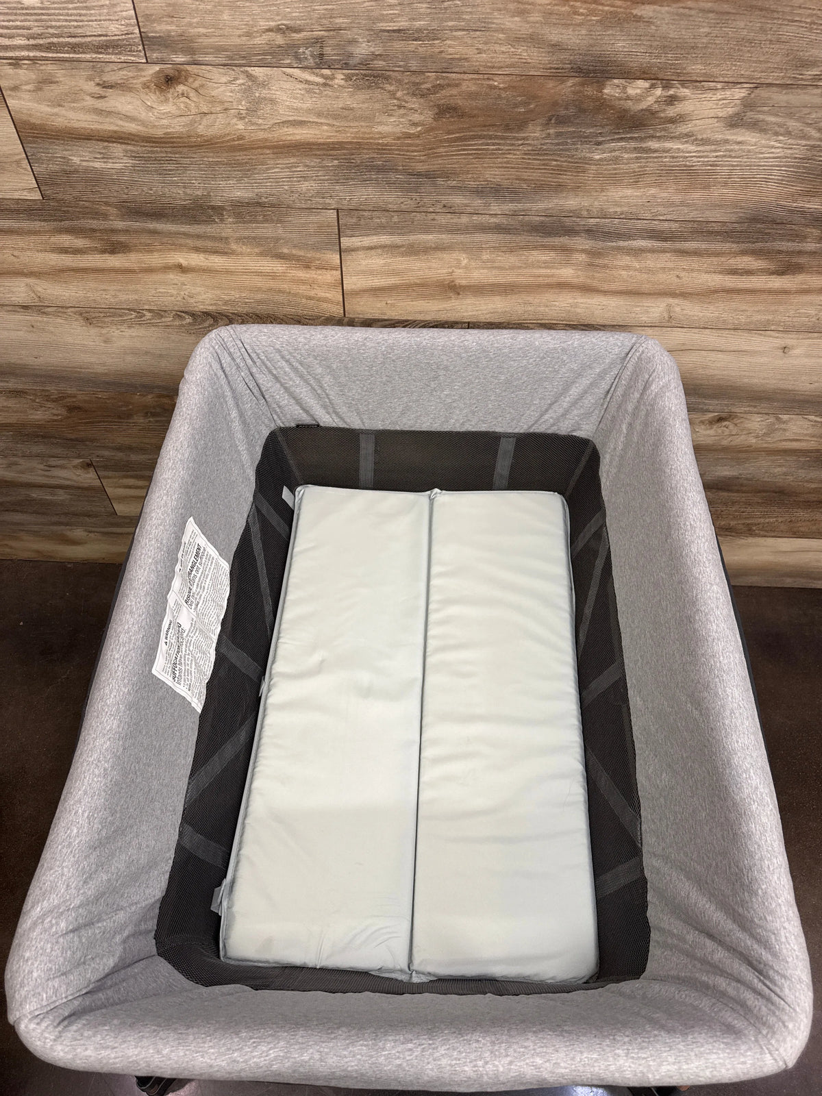 Top view of Maxi-Cosi Swift Playard in grey showcasing black mesh sides and a padded mattress on a wood floor