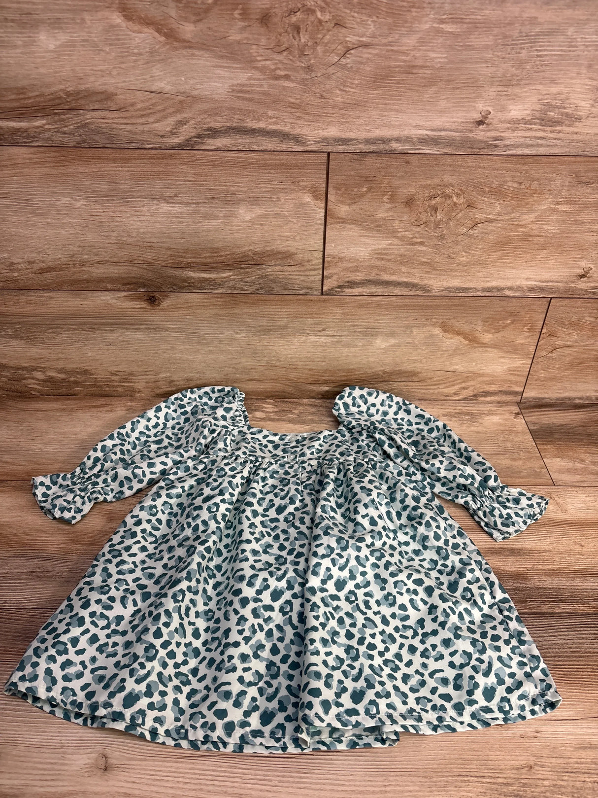 Long-sleeve baby dress with green leopard print on light background laid on wooden floor