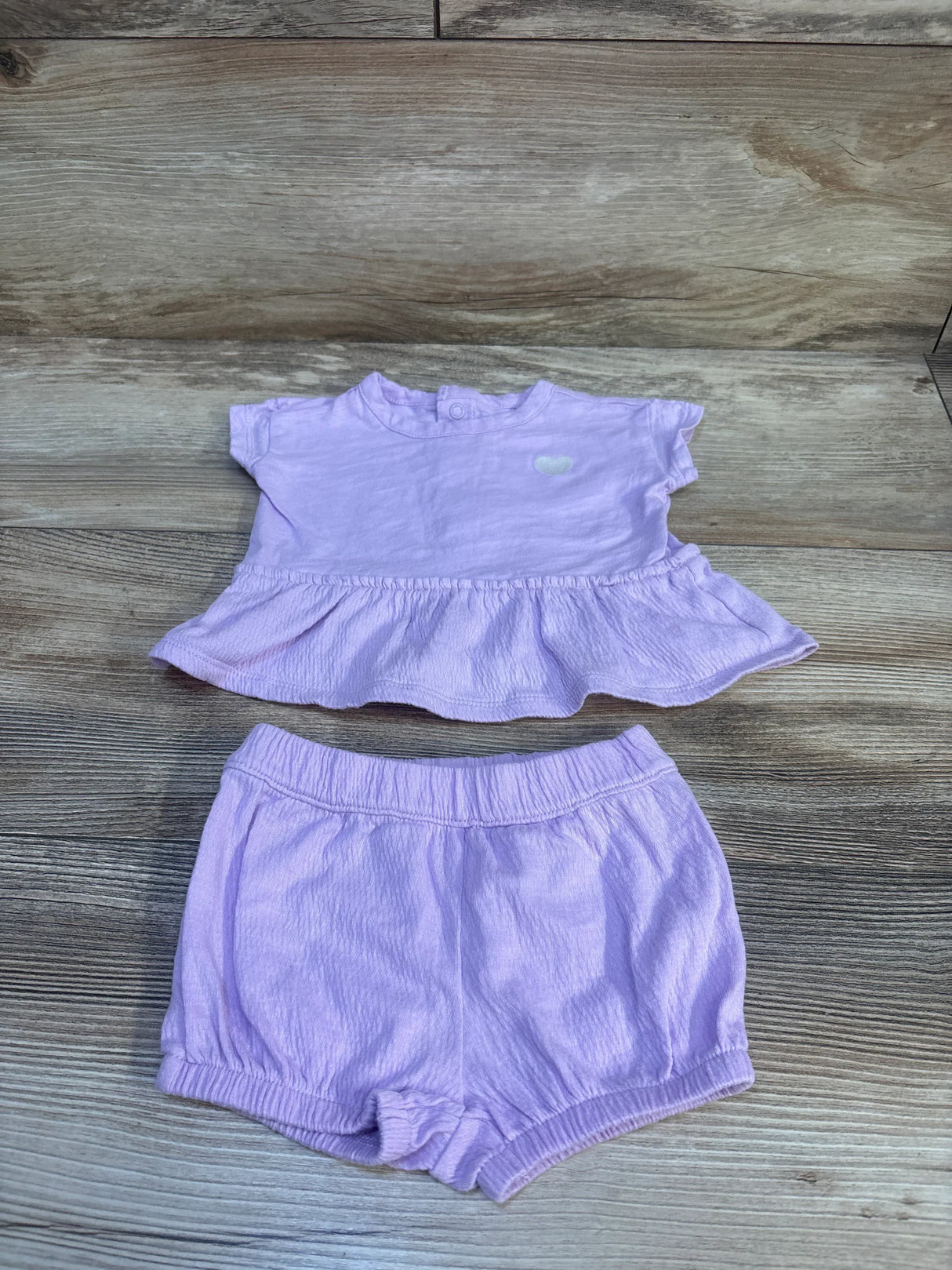 Flat lay of Carter’s lavender 2-piece peplum top and shorts, 3M, showing ruffled hem and elastic waistband on wood background