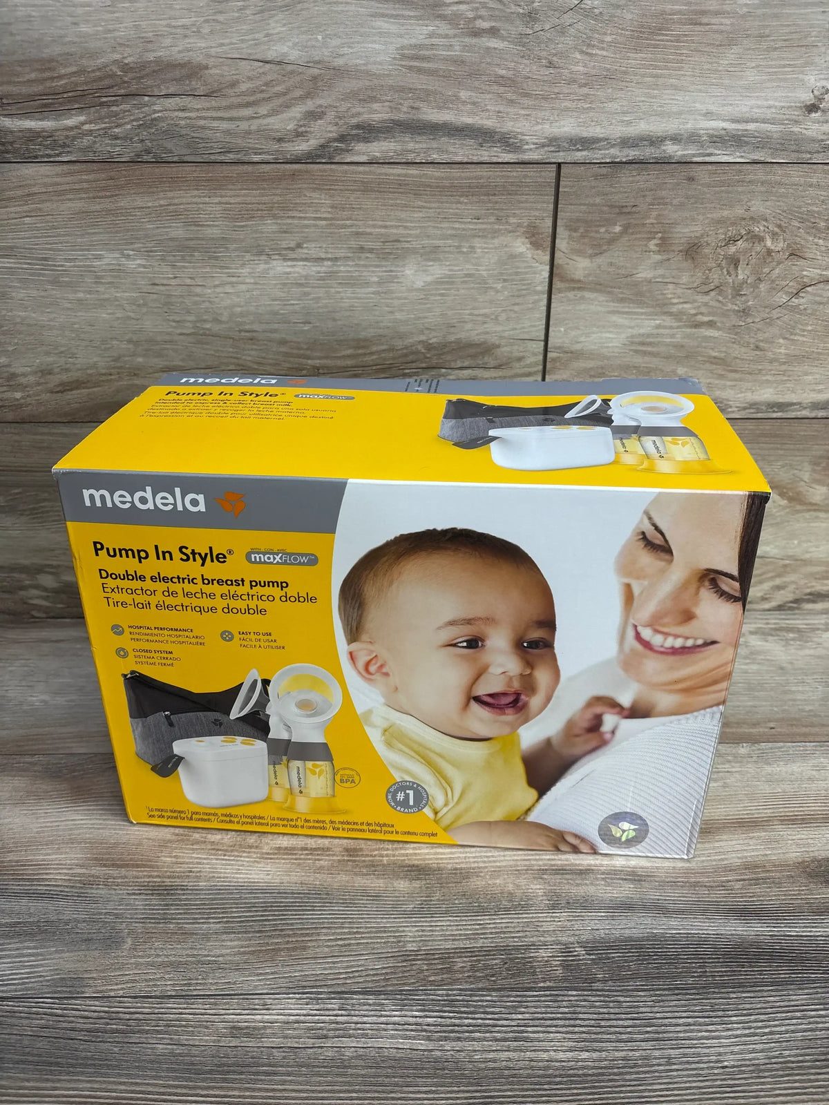 Front view of Medela Pump In Style double electric breast pump boxed kit showing pump unit, two bottles and gray carrying bag on wood background