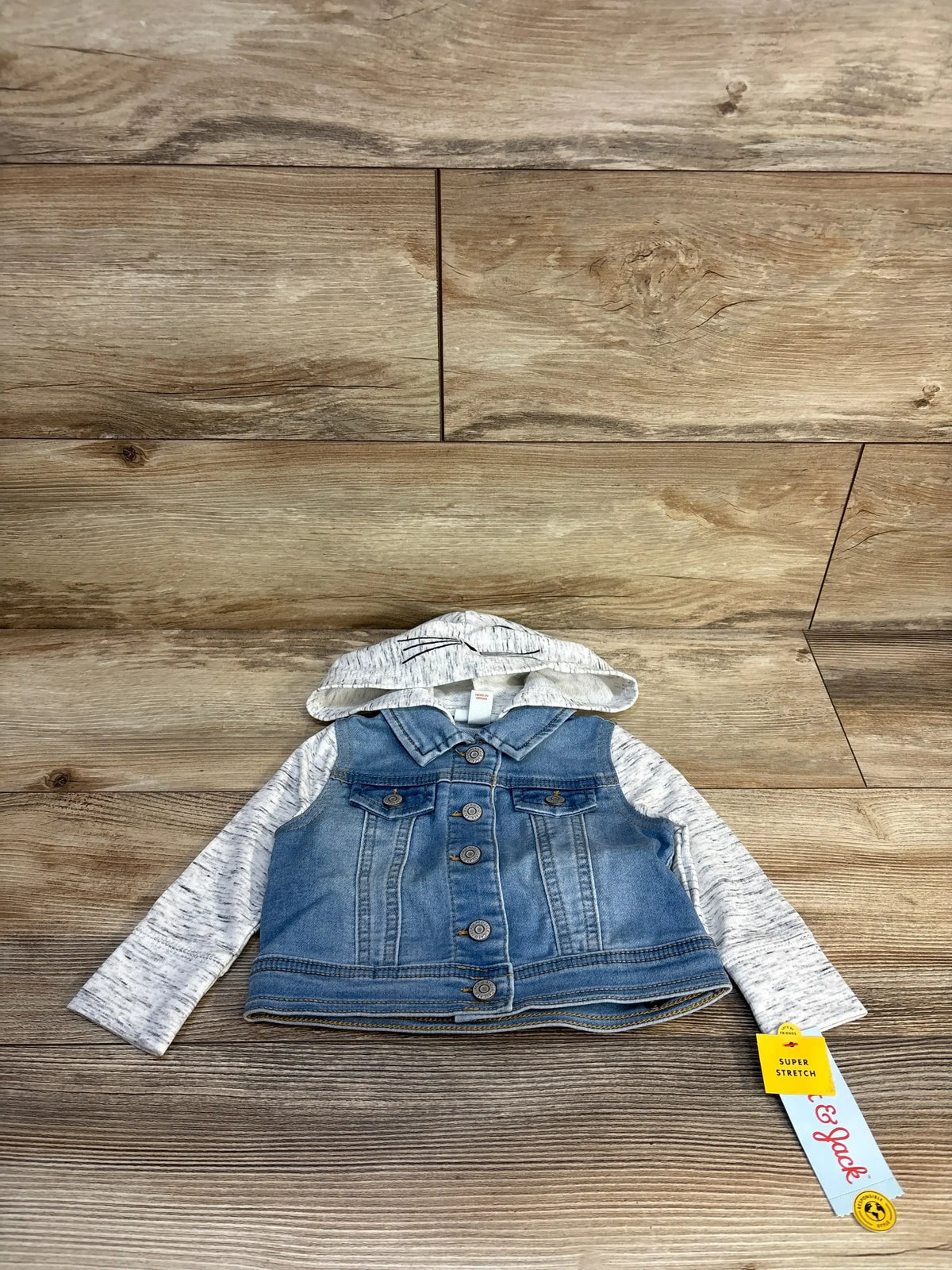 Front view of Cat and Jack girls’ hooded medium-wash denim jacket with button front and gray knit sleeves on wood background